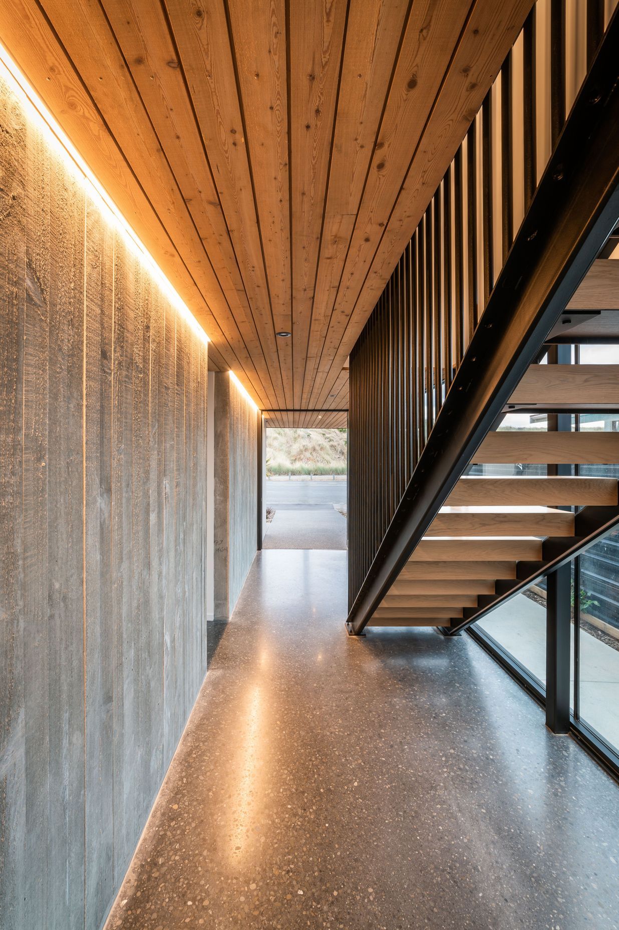 A board form concrete wall, larch ceiling and and black steel balustrades define the lower hallway