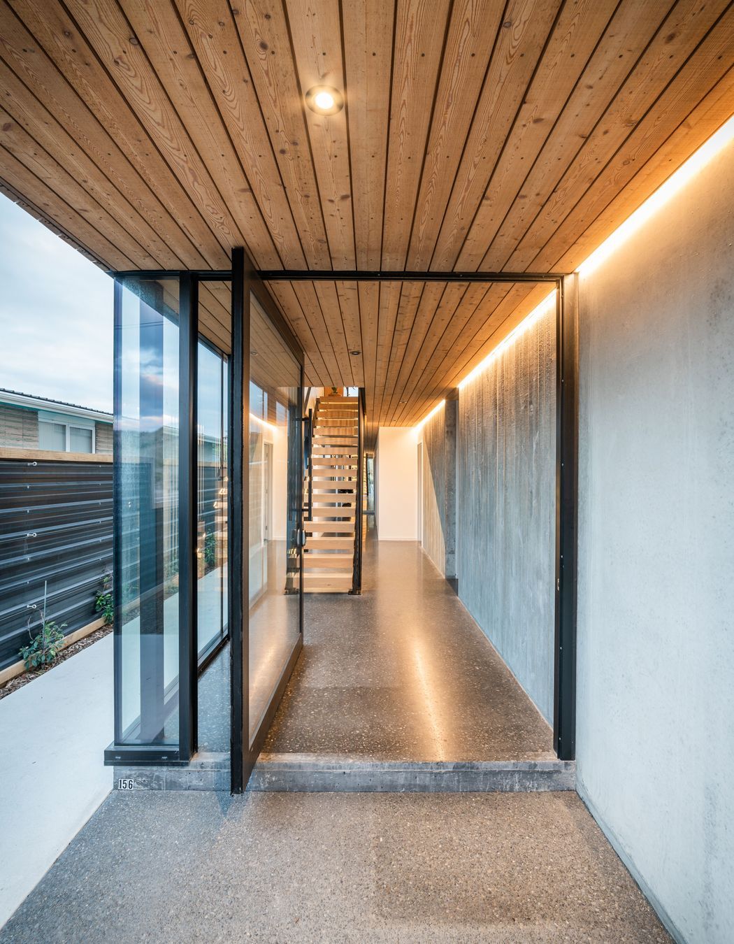 The steel-framed entrance door opens to a material palette that continues seamlessly from exterior to interior.