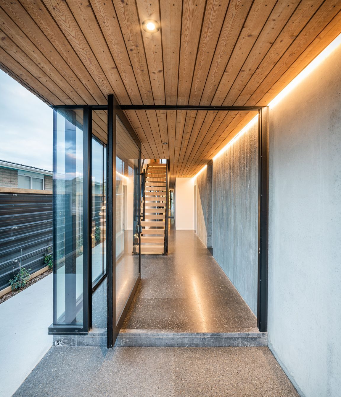 The steel-framed entrance door opens to a material palette that continues seamlessly from exterior to interior. 