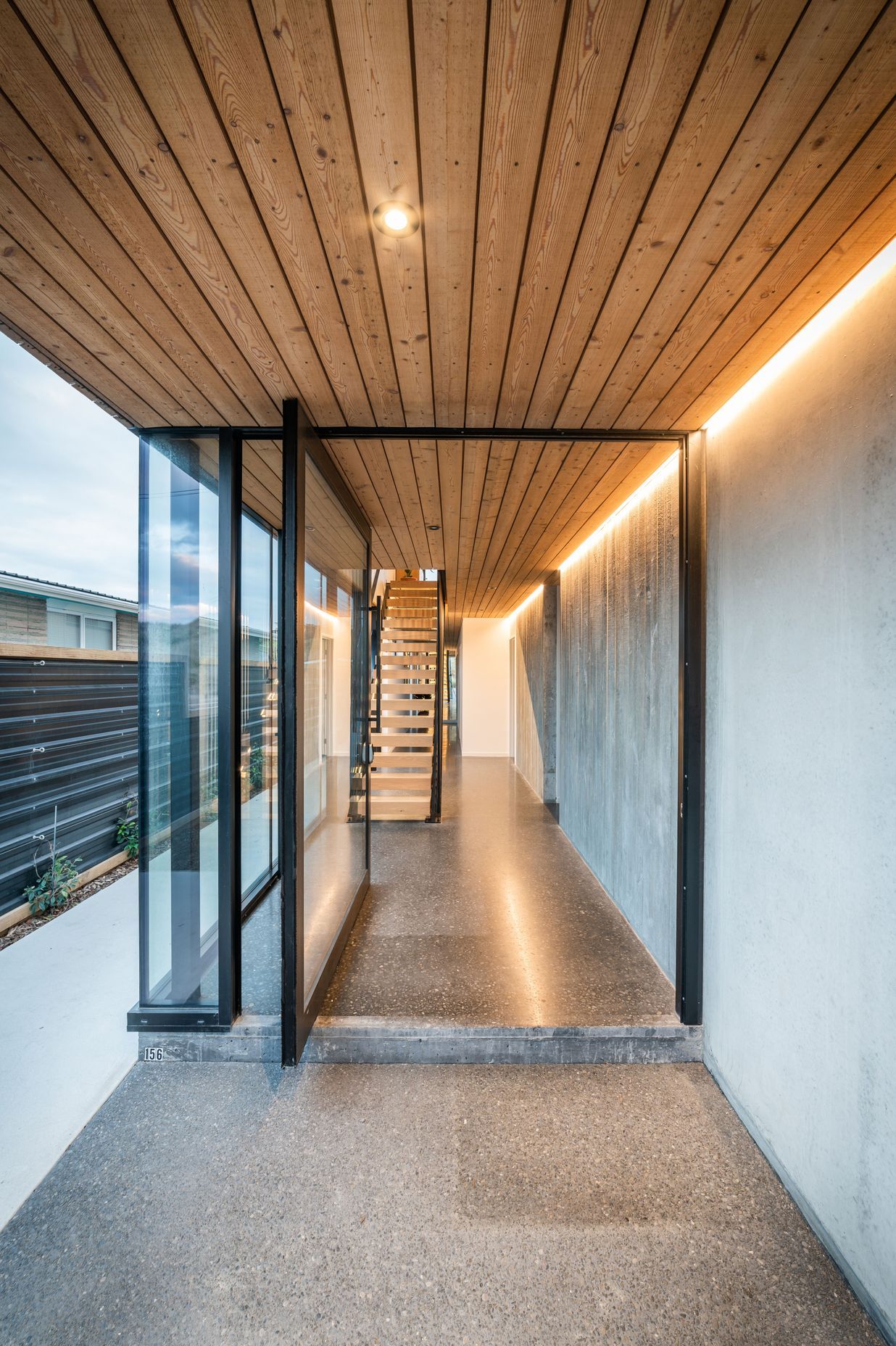 The steel-framed entrance door opens to a material palette that continues seamlessly from exterior to interior.