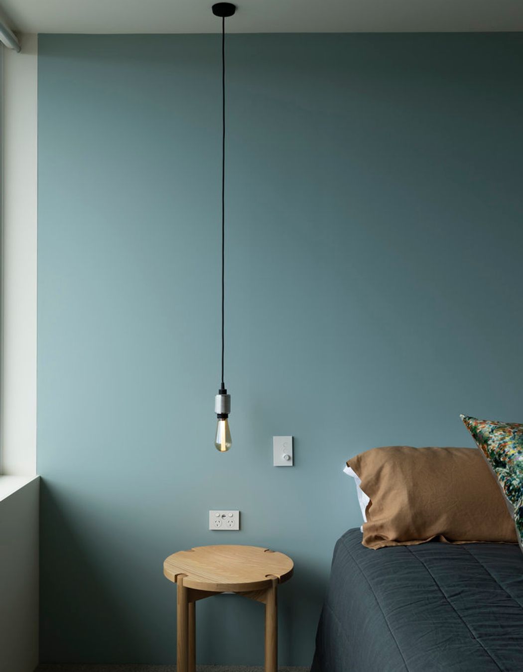 A simple low-hanging lightbulb provides bedside lighting.