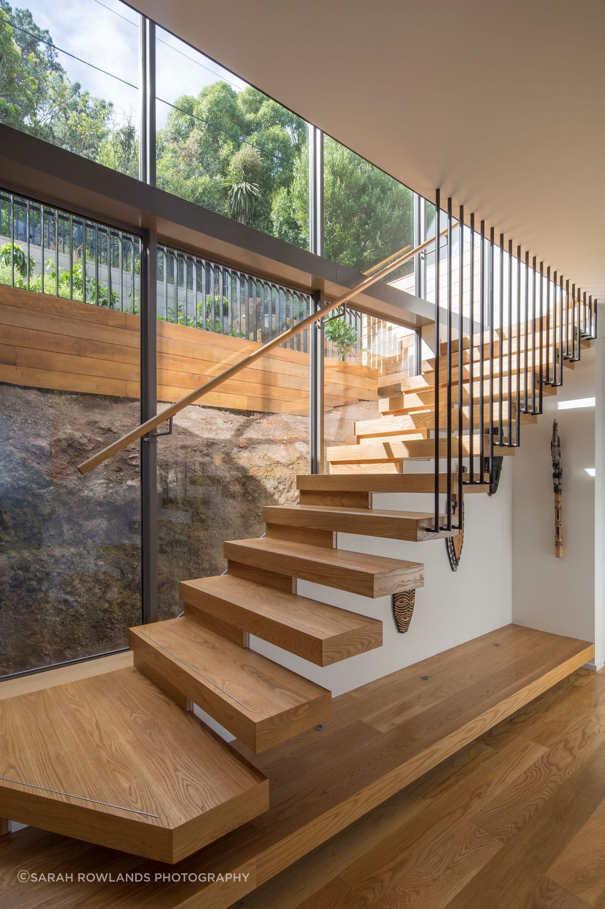 Double-height glazing behind the main, cantilevered, staircase shows how the house is sitting shy of the rockface behind.