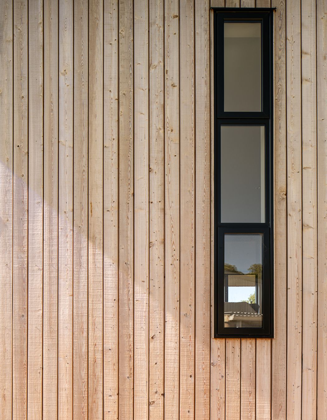 Tall, narrow windows on the western elevation are framed with black joinery.