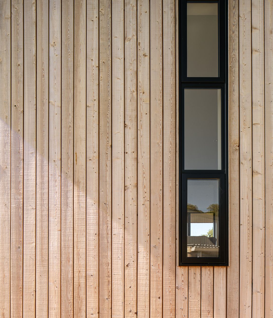 Tall, narrow windows on the western elevation are framed with black joinery.