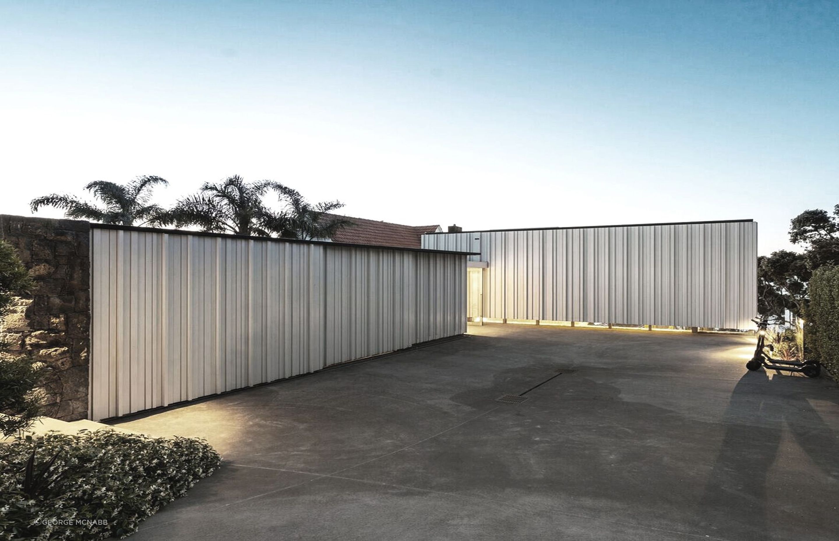 The main entrance is located at the back of the house, which is entered from the road at the top of a steep site. From here, the upper level of the form appears to float, with clerestory windows offering a sneaky peek into the interior of the home.