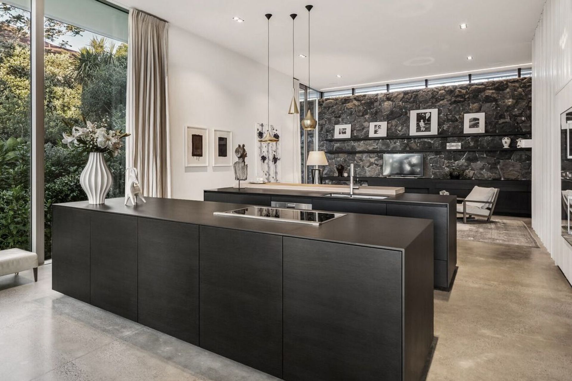 The view through the kitchen to the back of the house, where a basalt stone retaining wall sits underneath a clerestory window that draws morning light into the family space. 
