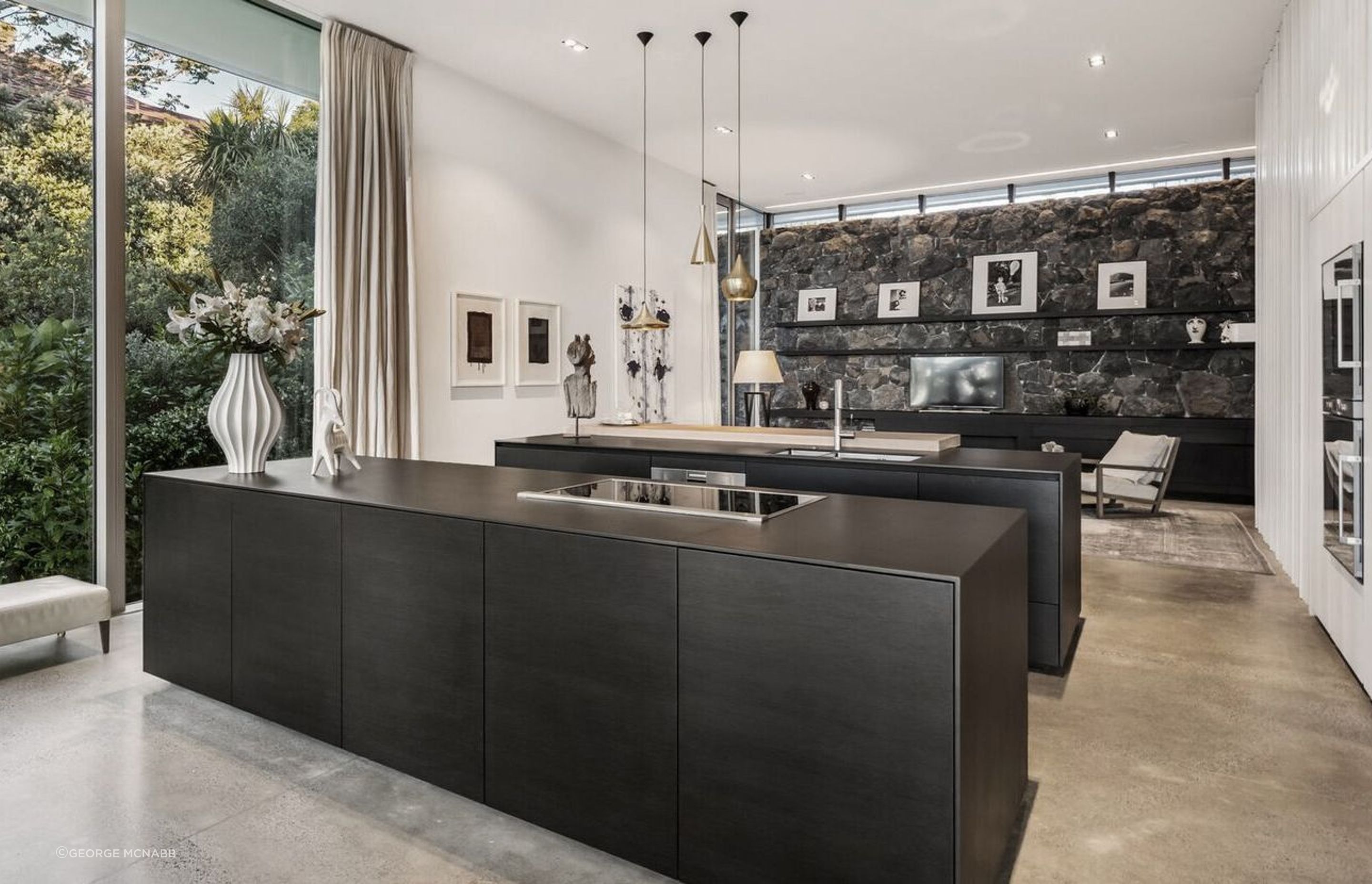 The view through the kitchen to the back of the house, where a basalt stone retaining wall sits underneath a clerestory window that draws morning light into the family space.