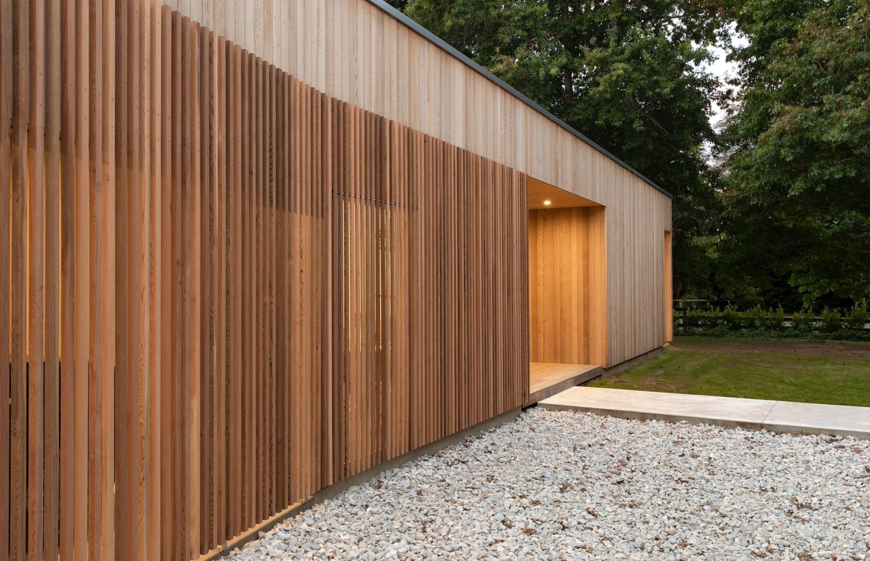 The main entrance is inset into the cedar-clad pavilion. A dramatic cedar rainscreen shields the carport from the road and filters light through the large office window.