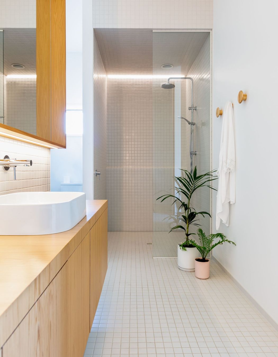 The bathroom is lined with white tiles and wall, to contrast the warm timber cabinetry.