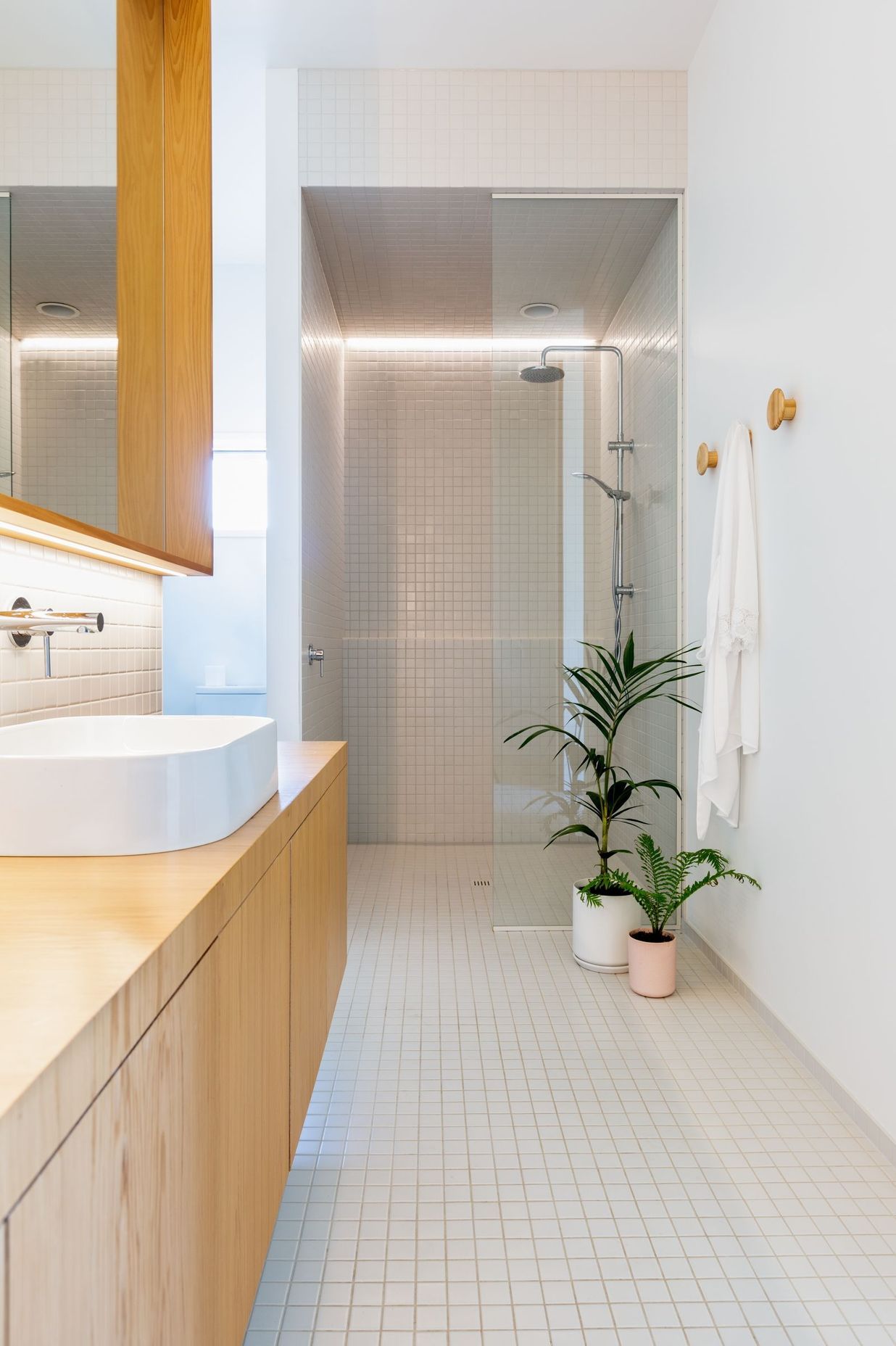 The bathroom is lined with white tiles and wall, to contrast the warm timber cabinetry.