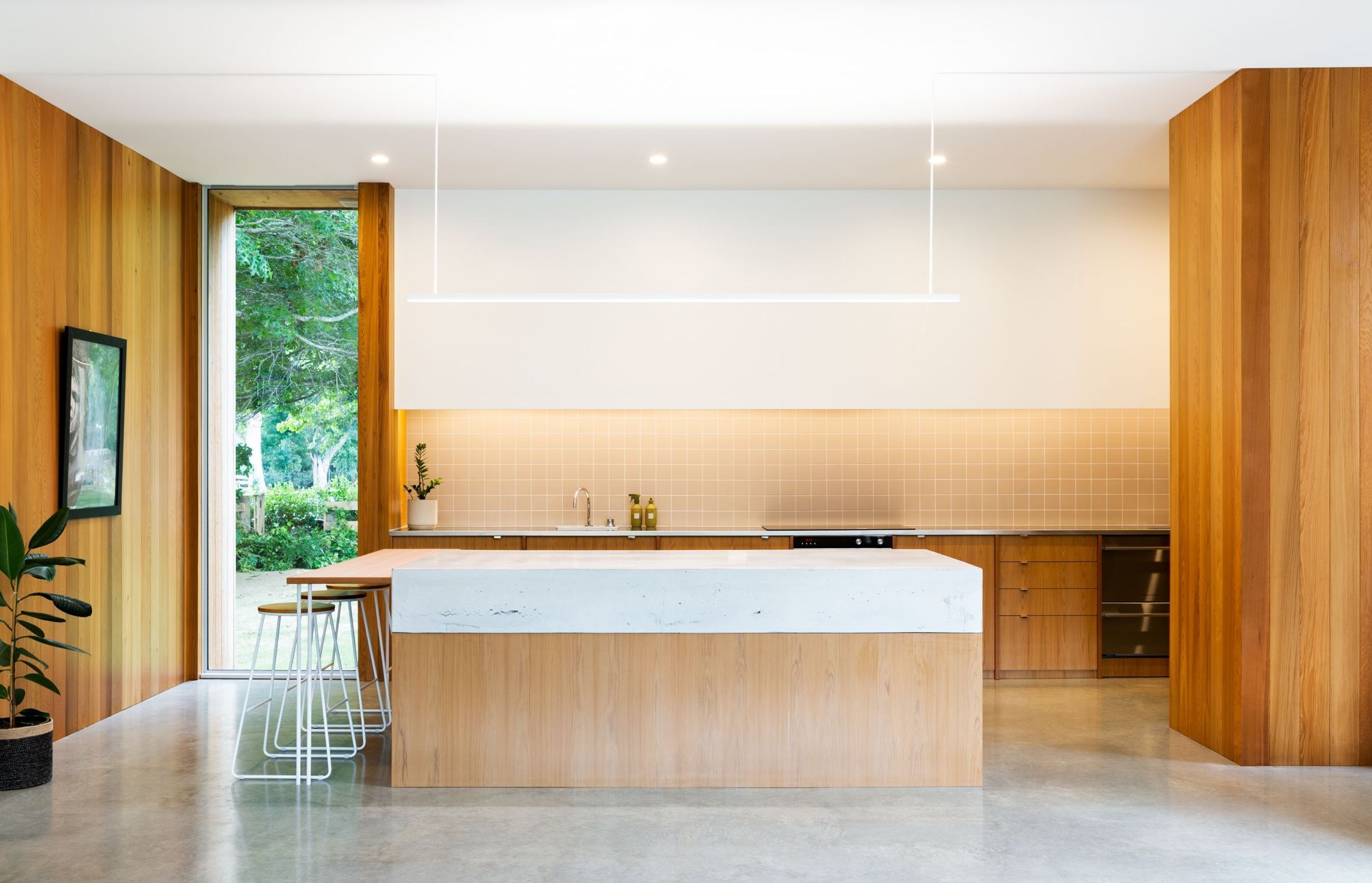 The minimalist kitchen contains accessible low-level cabinetry, with the pantry, oven and fridge hidden behind. The breakfast bar stools avoid dominating the front of the island.