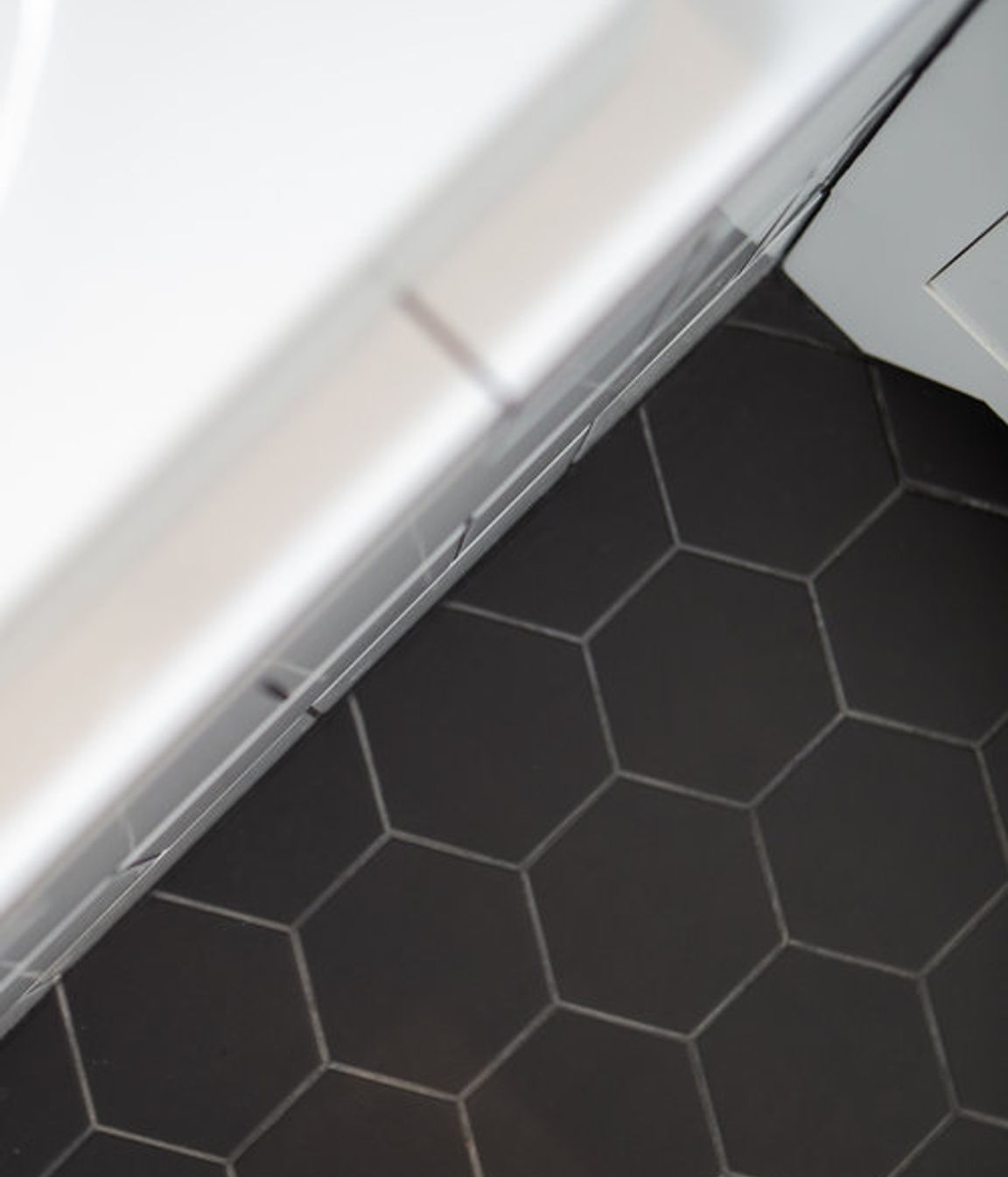 Black hexagonal tiles on the floor are contrasted with gloss white and dark grout on the walls and bath.