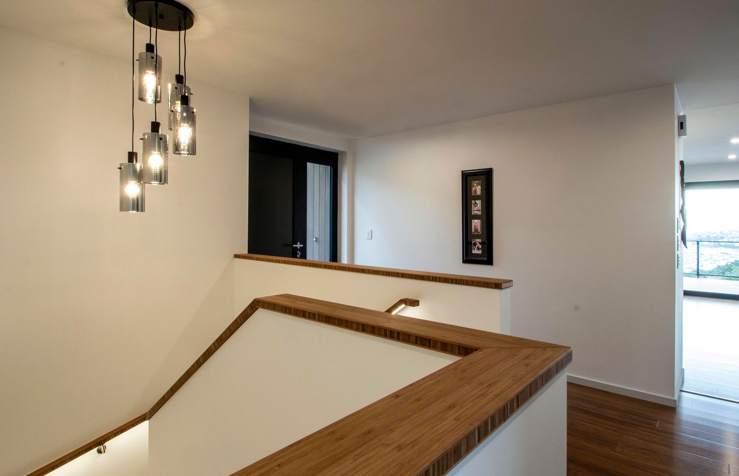 White walls, bamboo ballastrades and a feature pendant are the features of the hallway and staircase which leads to the lower level.