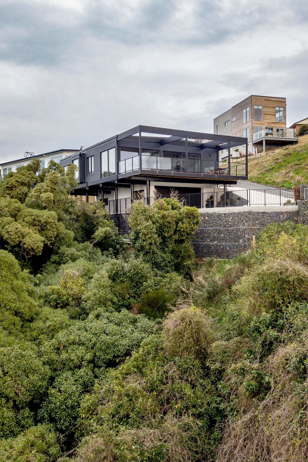 The house sits into the hillside, supported by a terraced gabion wall.