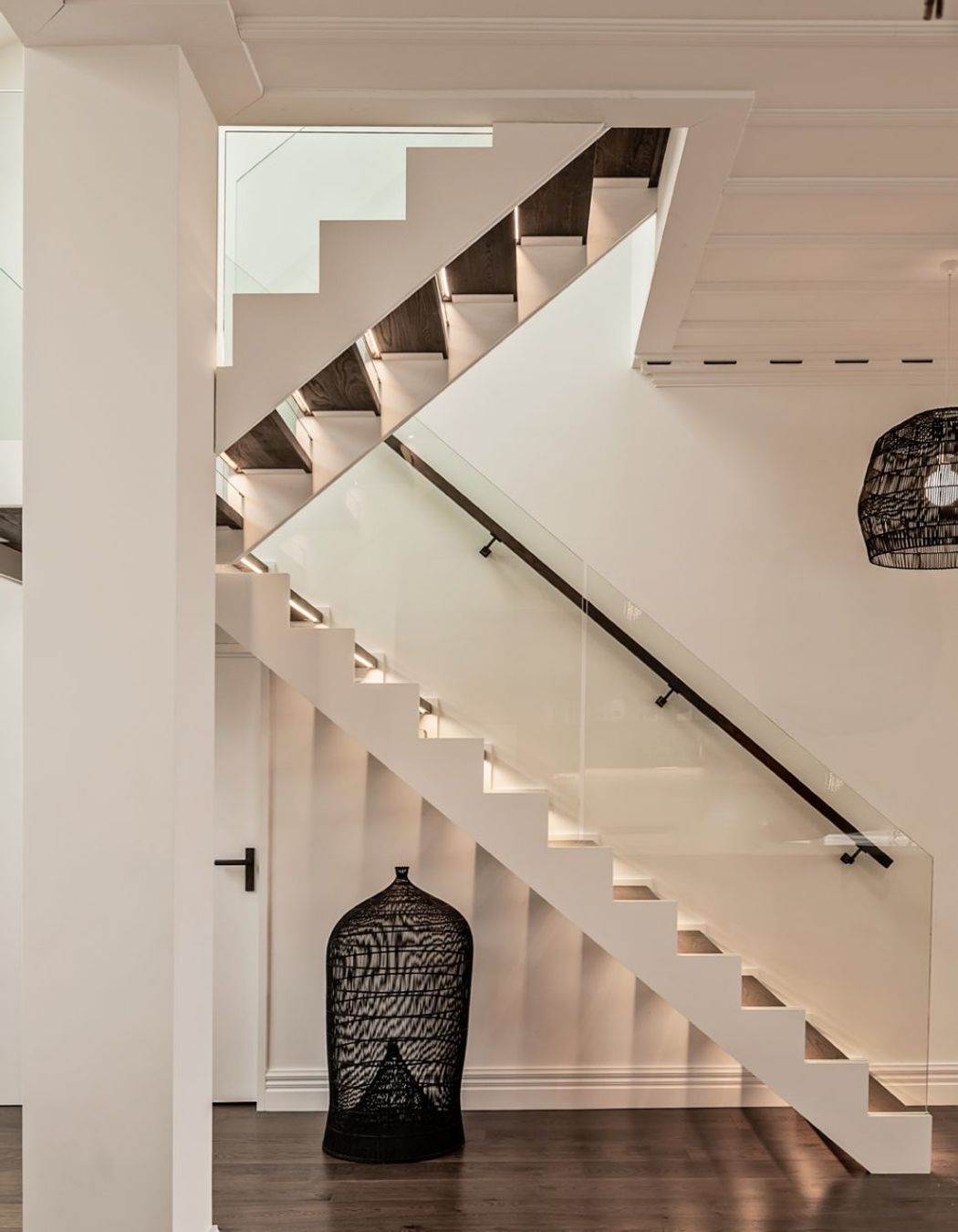 A modern staircase has dark oak treads to match the flooring and glass balustrades.