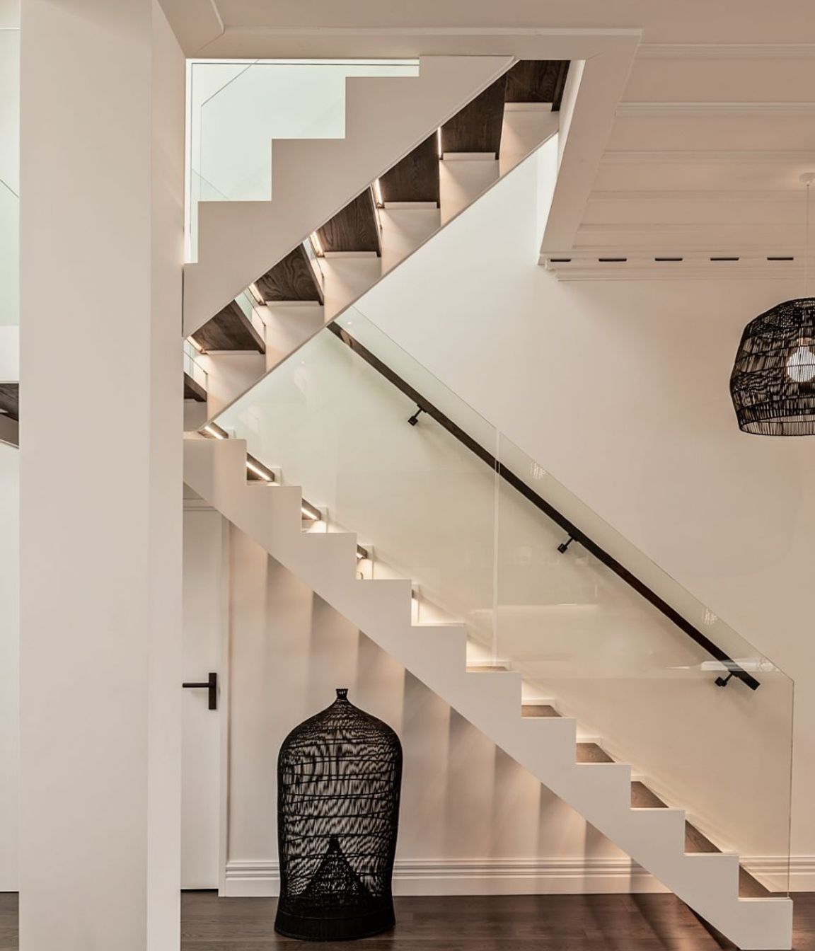 A modern staircase has dark oak treads to match the flooring and glass balustrades.