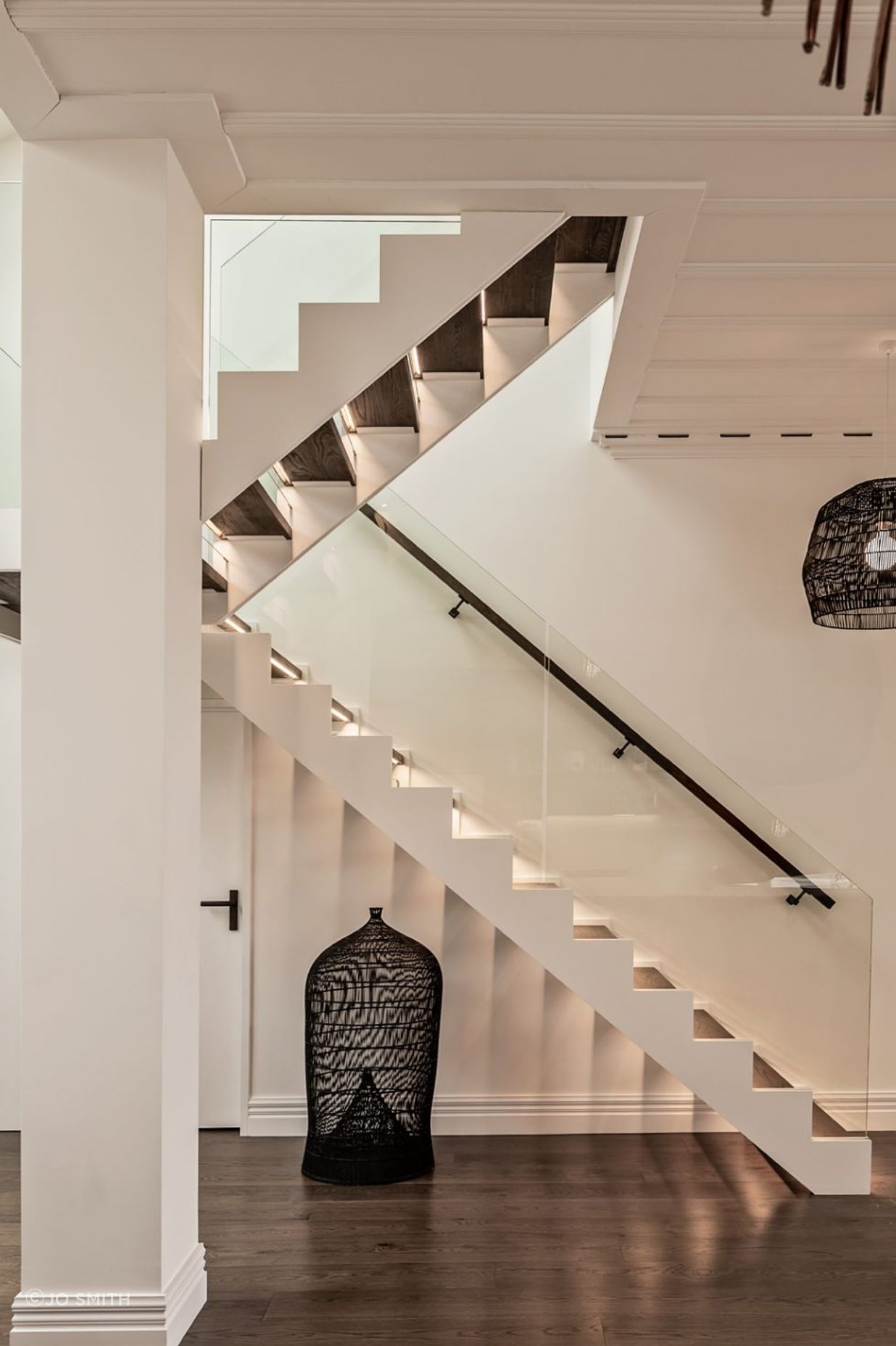 A modern staircase has dark oak treads to match the flooring and glass balustrades.