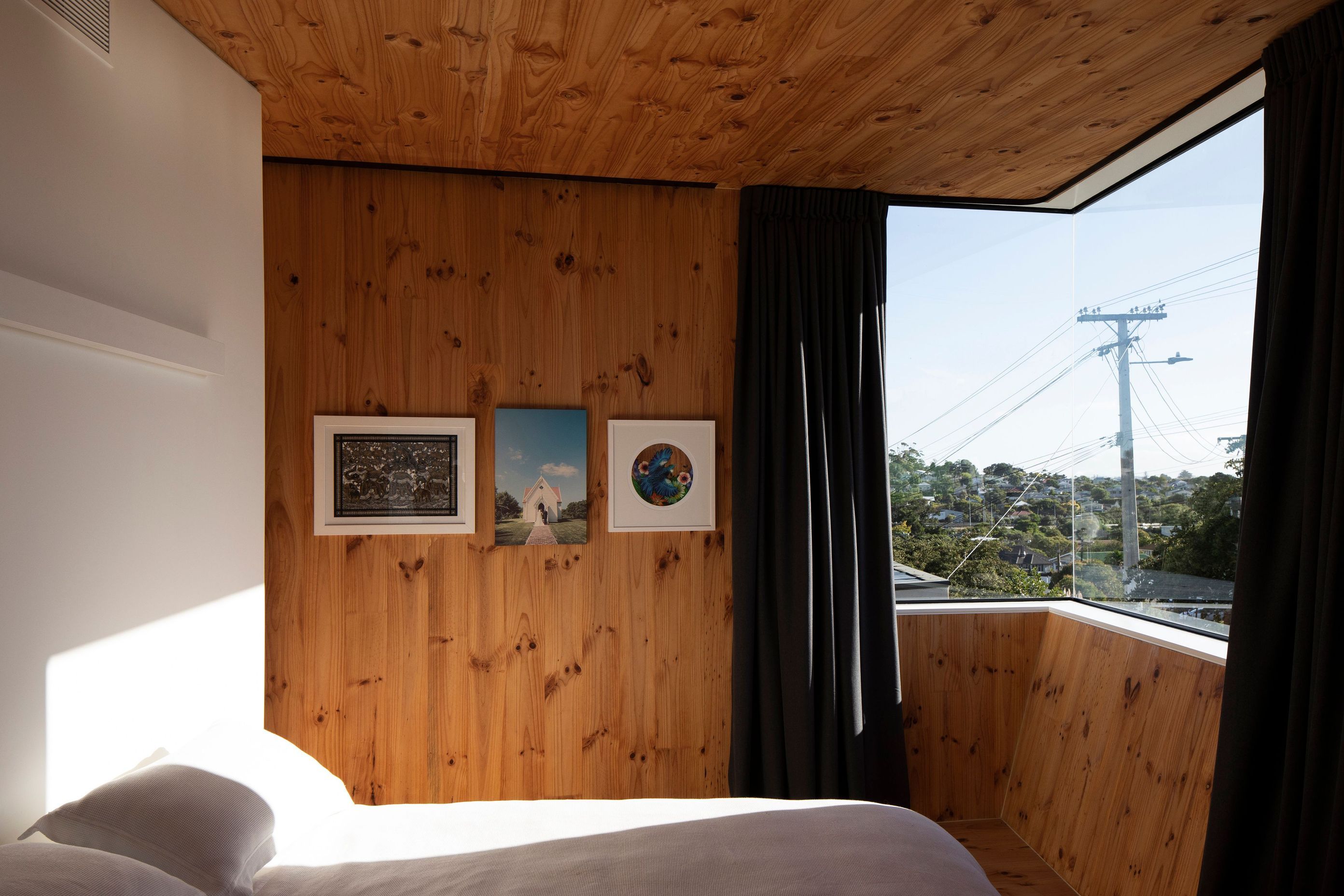 The timber-clad master bedroom has a corner window facing the Waitakere Ranges and unusual angled walls.