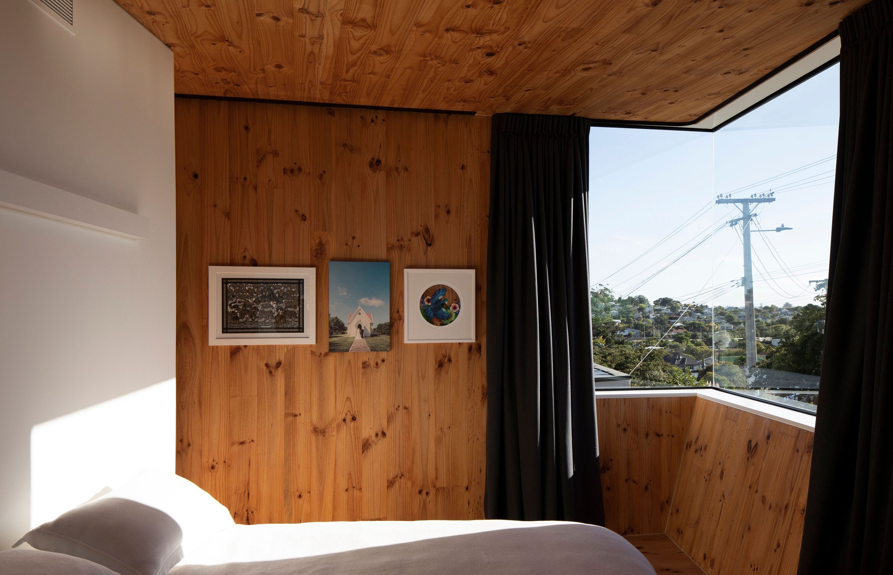 The timber-clad master bedroom has a corner window facing the Waitakere Ranges and unusual angled walls.