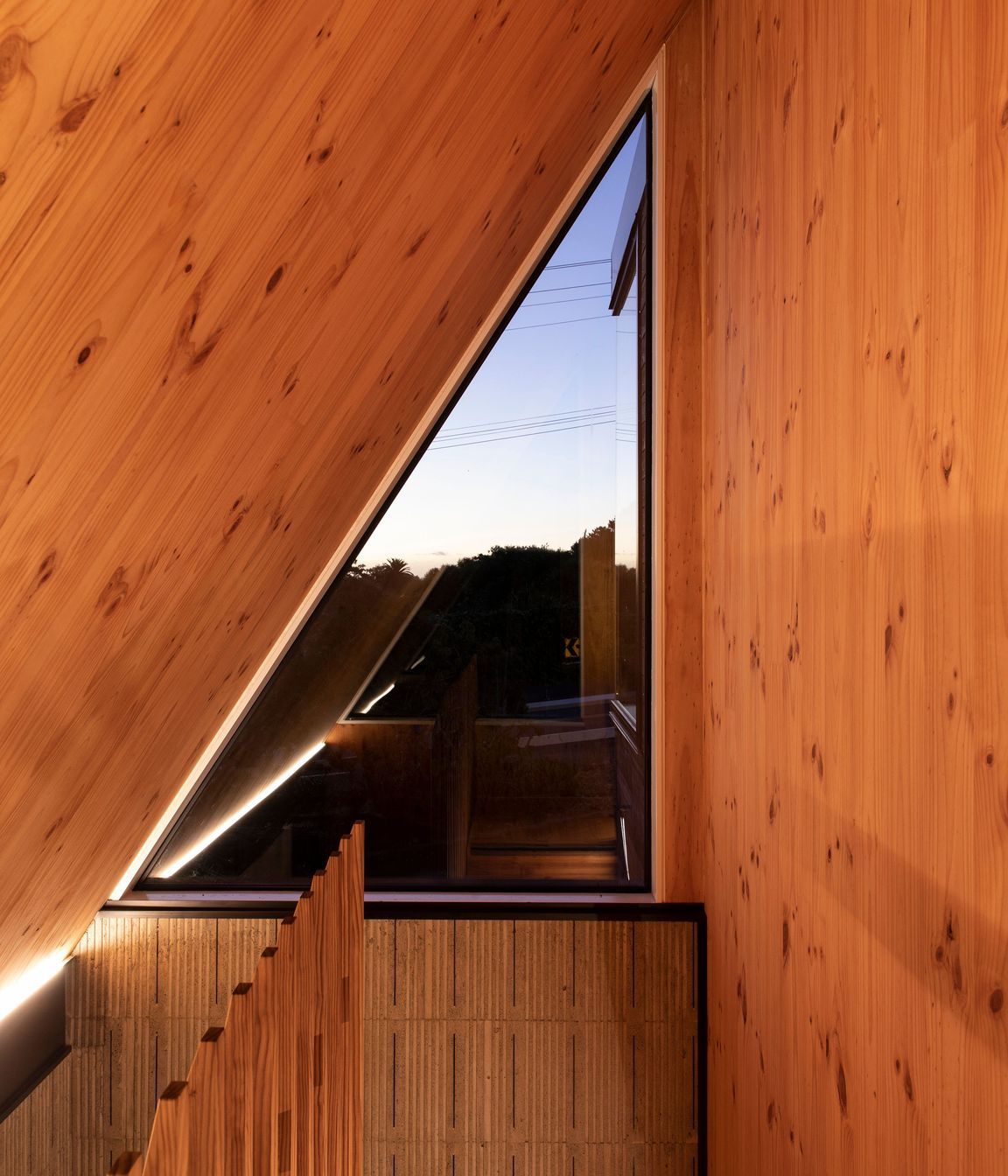 A high triangular window at the top of the stairs is surrounded by New Zealand pine.