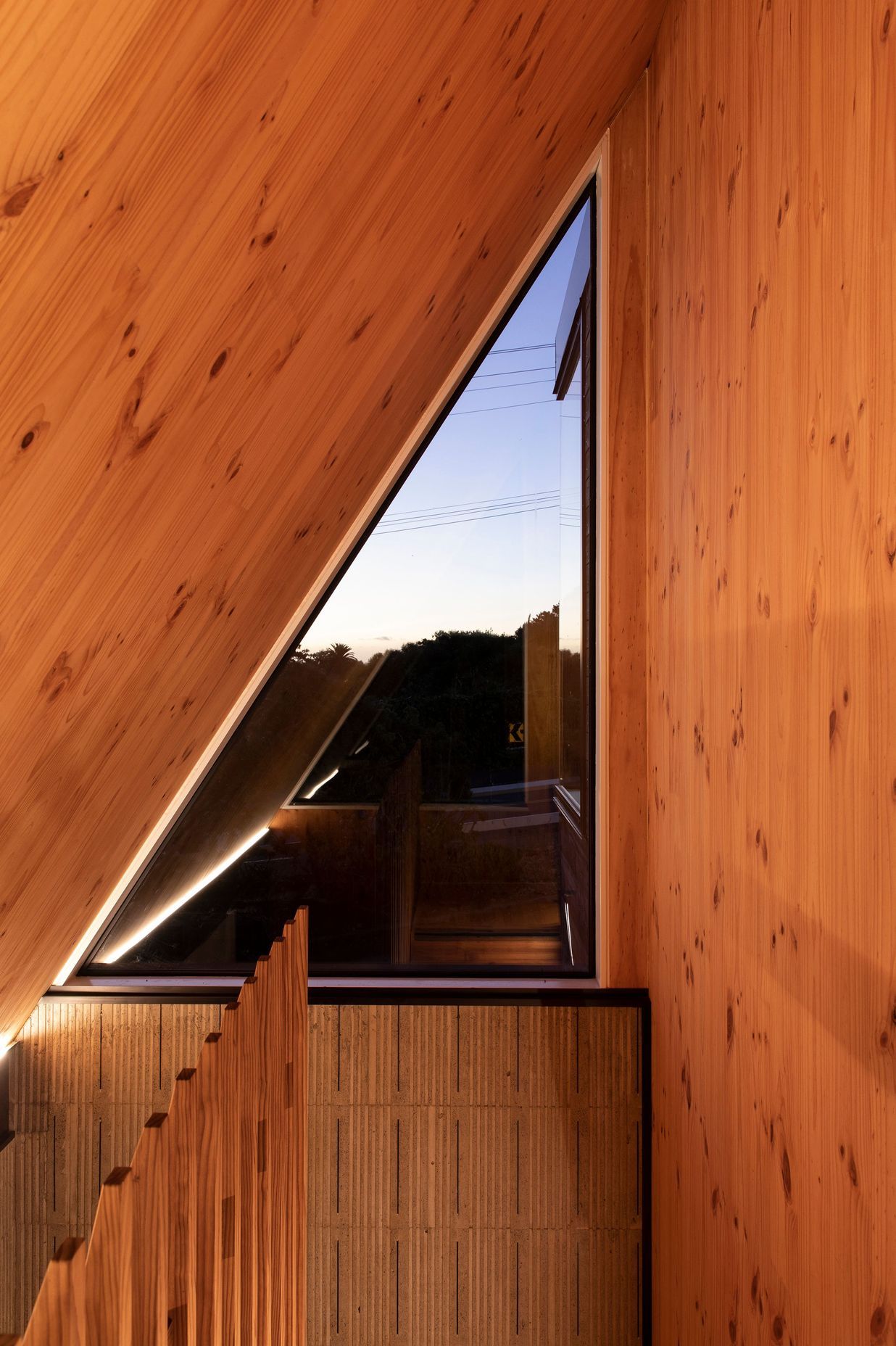 A high triangular window at the top of the stairs is surrounded by New Zealand pine.