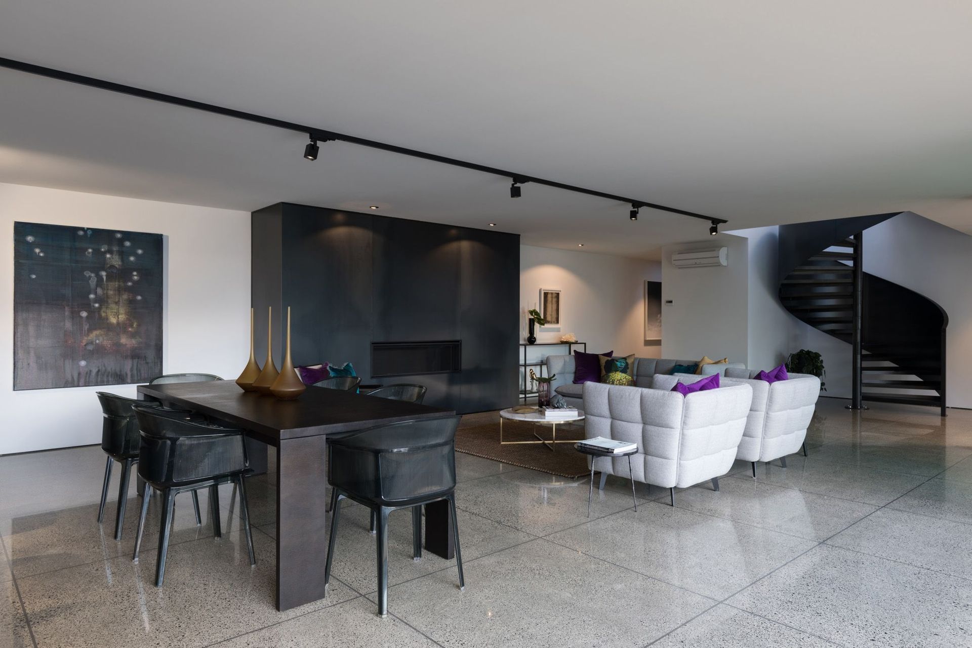 The monochromatic dining/living area winds up to the upper floor via a spiral staircase. Large tiles are a functional flooring material suited to coastal living.
