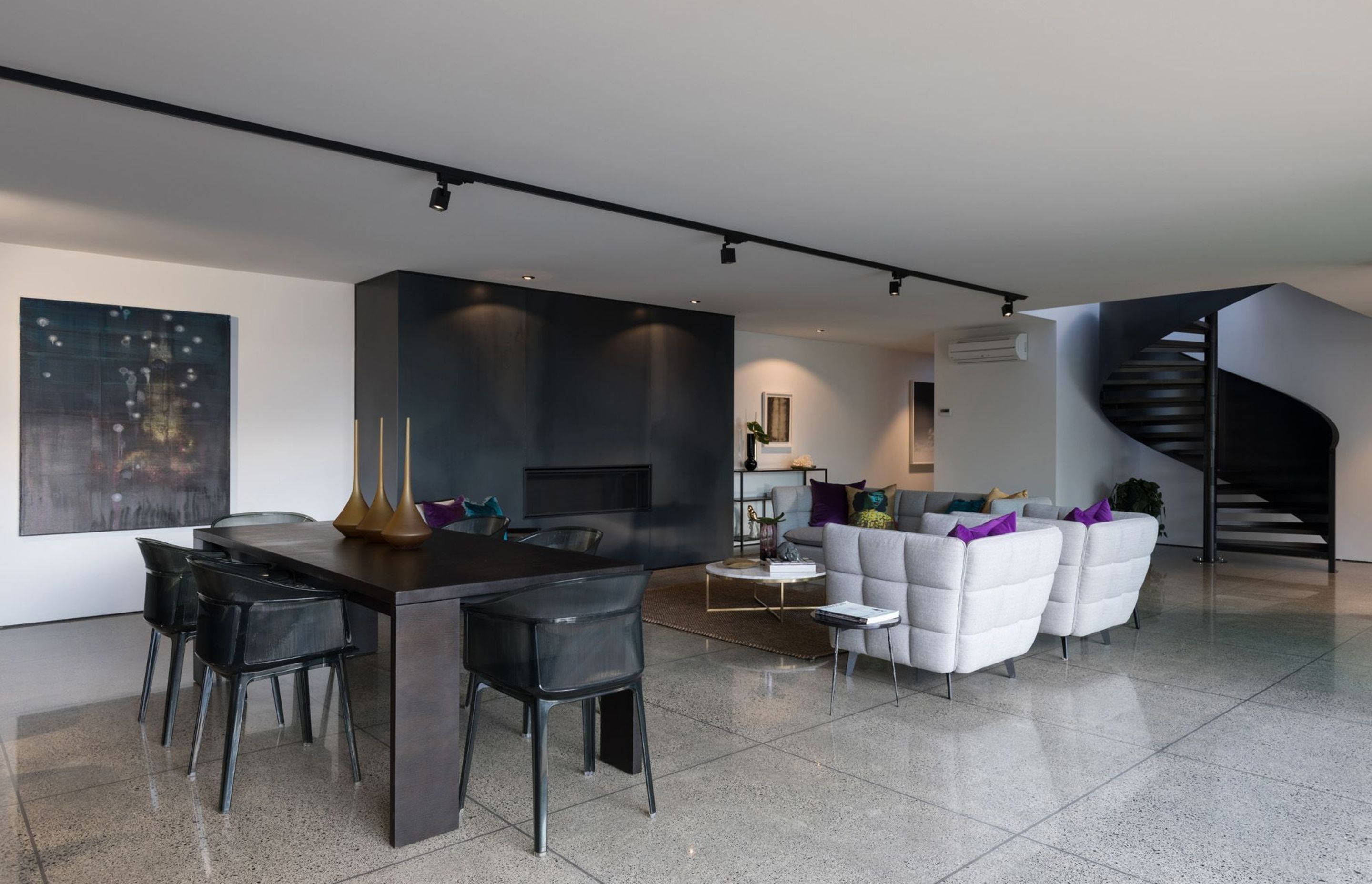 The monochromatic dining/living area winds up to the upper floor via a spiral staircase. Large tiles are a functional flooring material suited to coastal living.