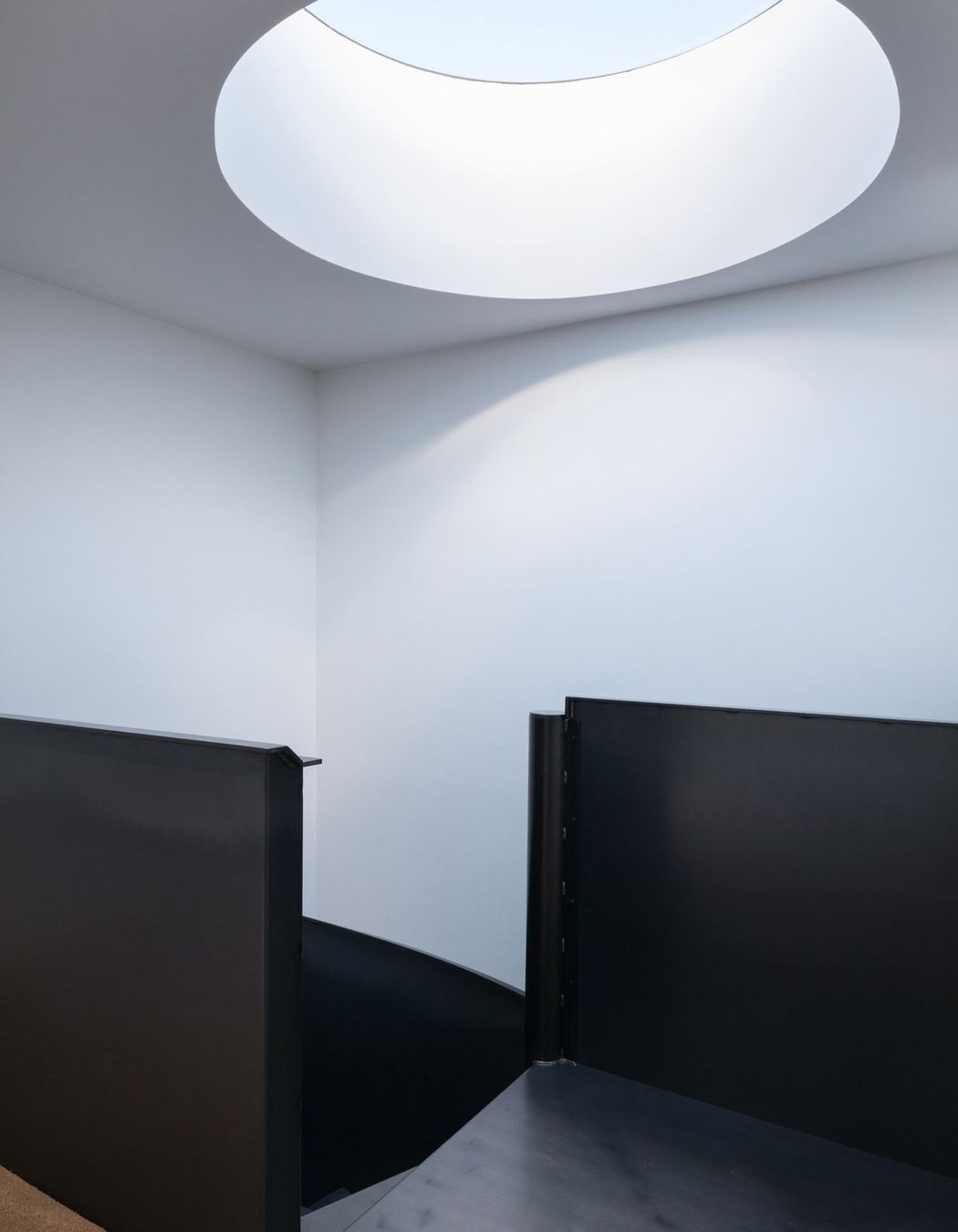 Black and white unite – an occulus in the ceiling floods light down over the staircase.