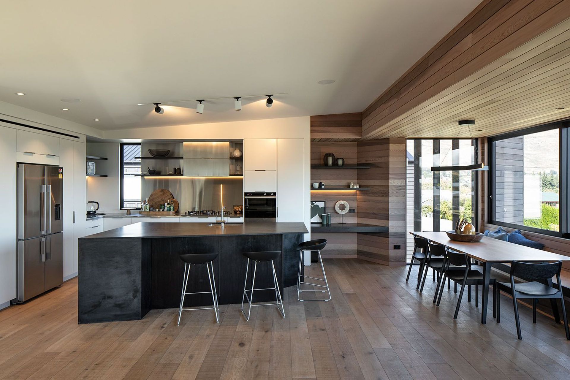 The monochromatic kitchen is complemented by wide-plank oak flooring, built-in cedar shelves and a lowered cedar ceiling over the dining area that runs out into the lounge wall and balcony soffit.