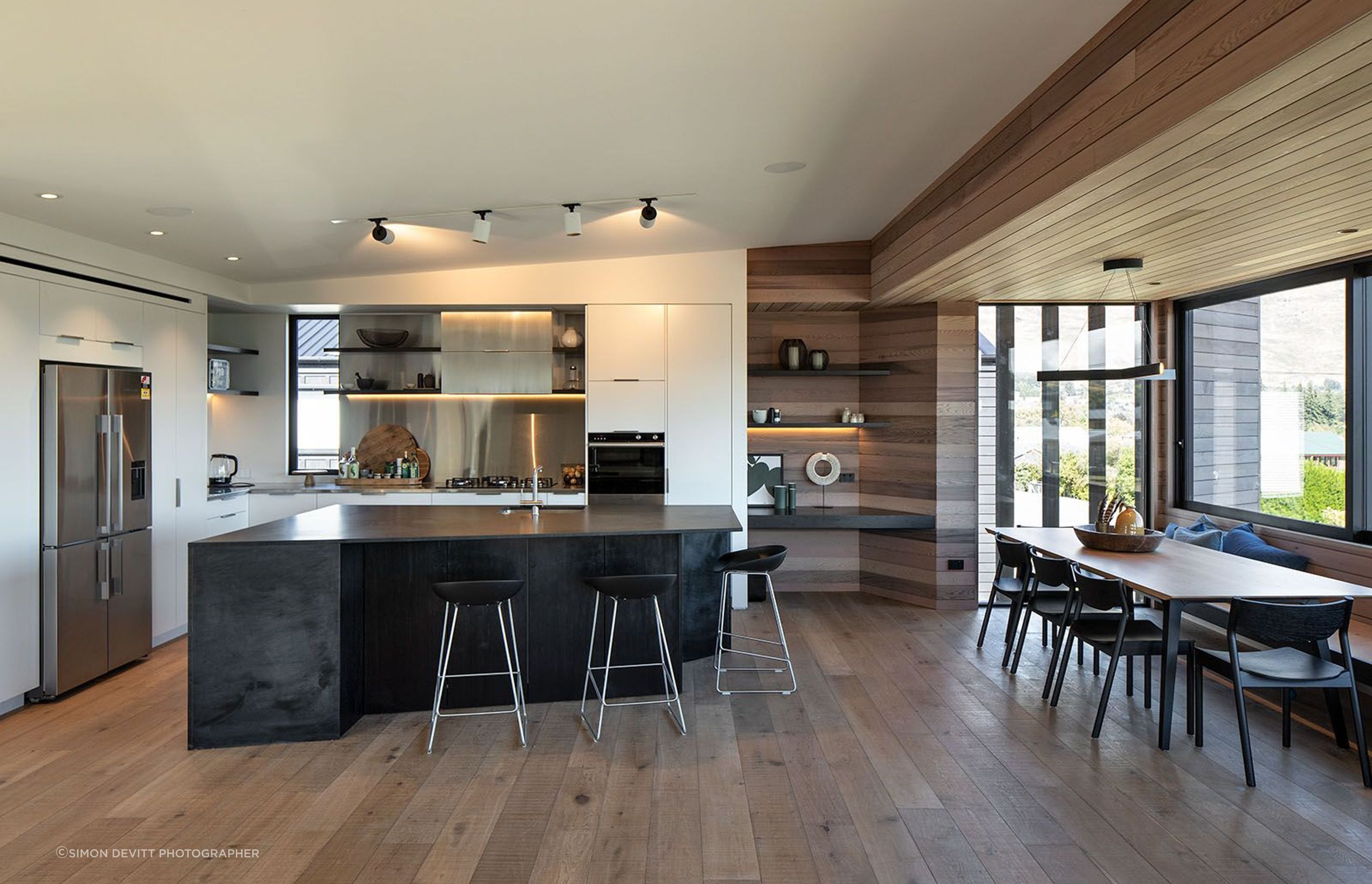 The monochromatic kitchen is complemented by wide-plank oak flooring, built-in cedar shelves and a lowered cedar ceiling over the dining area that runs out into the lounge wall and balcony soffit.