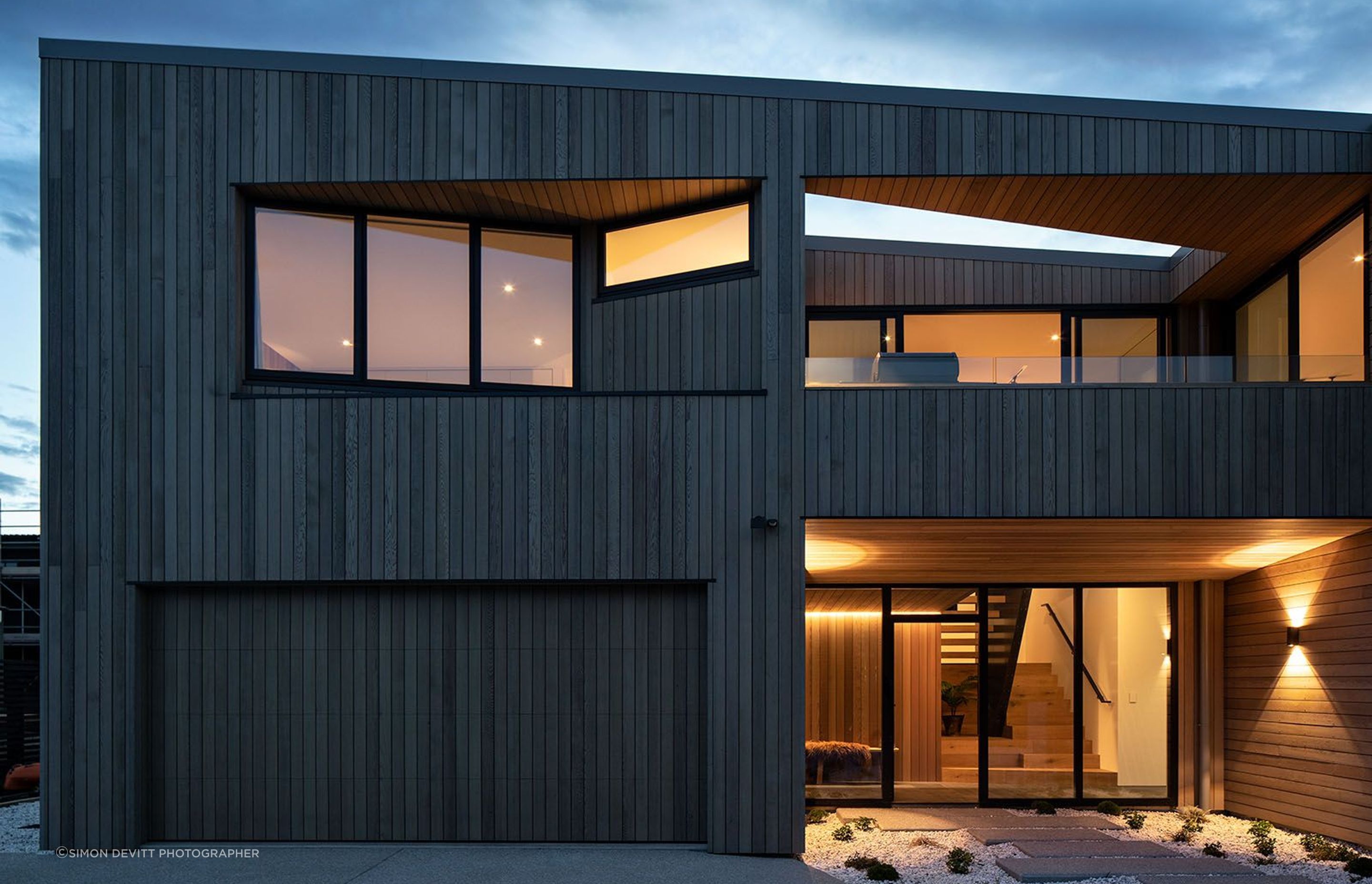 A night image of the east-facing elevation showing the main entrance and garage doors below and the morning deck above.