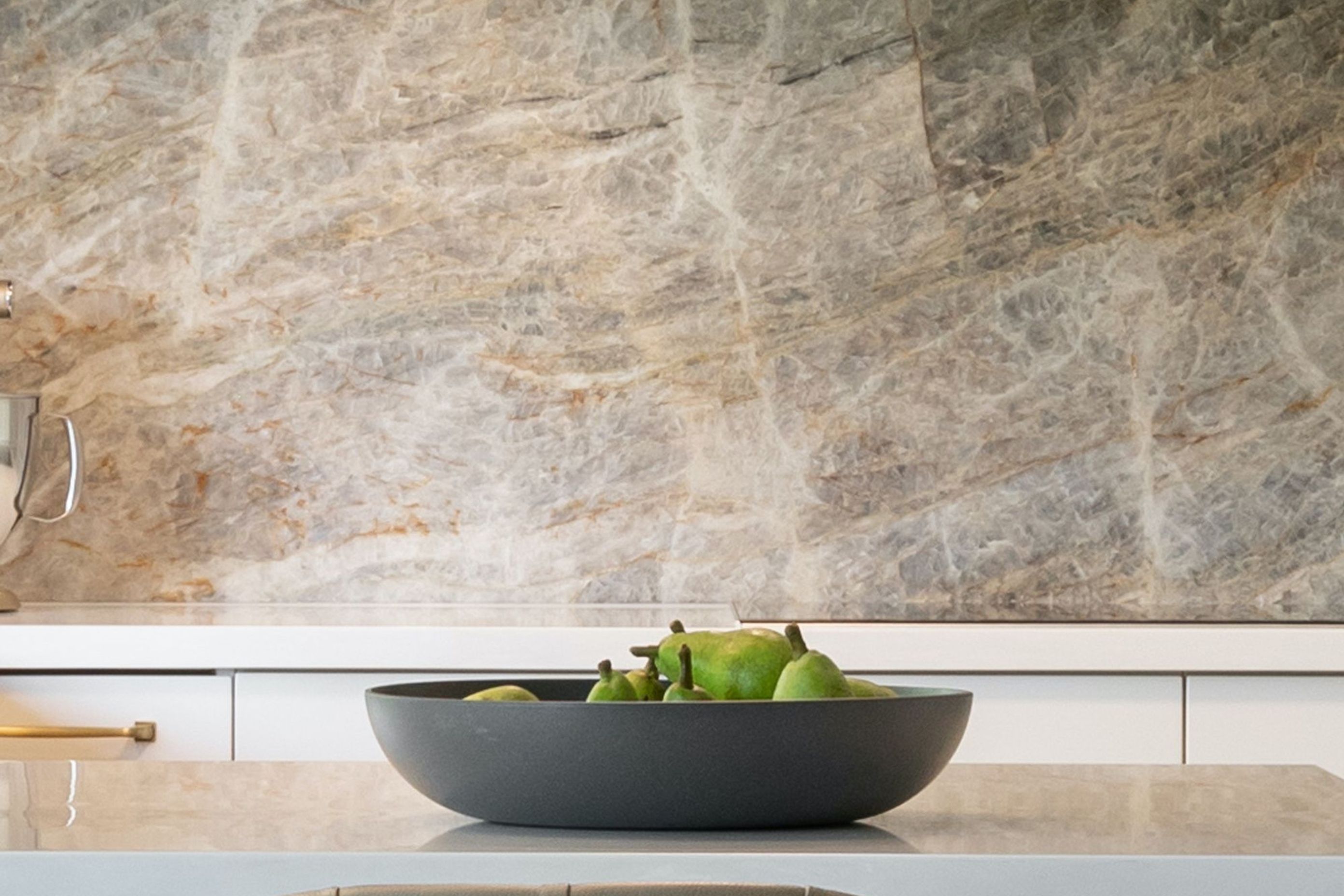 A beauty of nature itself, the stunning “Cielo” quartzite wall treatment draws the eye into its beautiful rich texture and colours. These colours inspire the kitchen’s aesthetics with contrasting dark &amp; light cabinetry and echos of gold. 