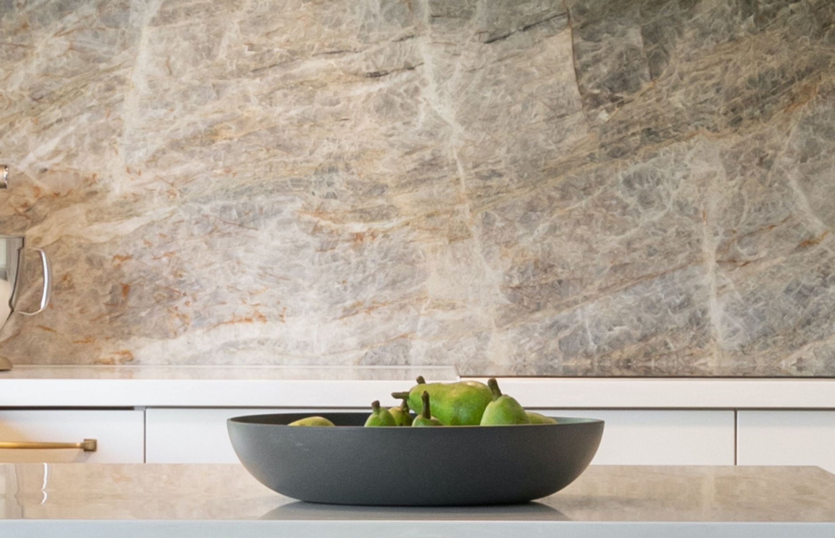 A beauty of nature itself, the stunning “Cielo” quartzite wall treatment draws the eye into its beautiful rich texture and colours. These colours inspire the kitchen’s aesthetics with contrasting dark &amp; light cabinetry and echos of gold. 