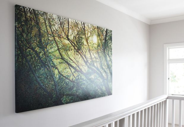 A bright interior landing or hallway with white walls, a white railing, and a large forest-themed artwork mounted on the wall. A window provides natural light, creating a clean and airy atmosphere. The architecture is simple and contemporary with minimal decorative detailing.