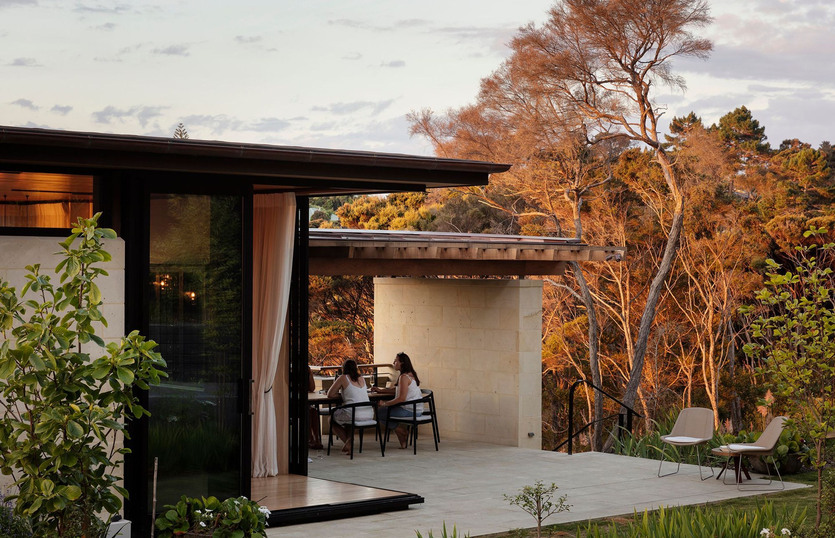 An outdoor room is sheltered between the house and established planting.