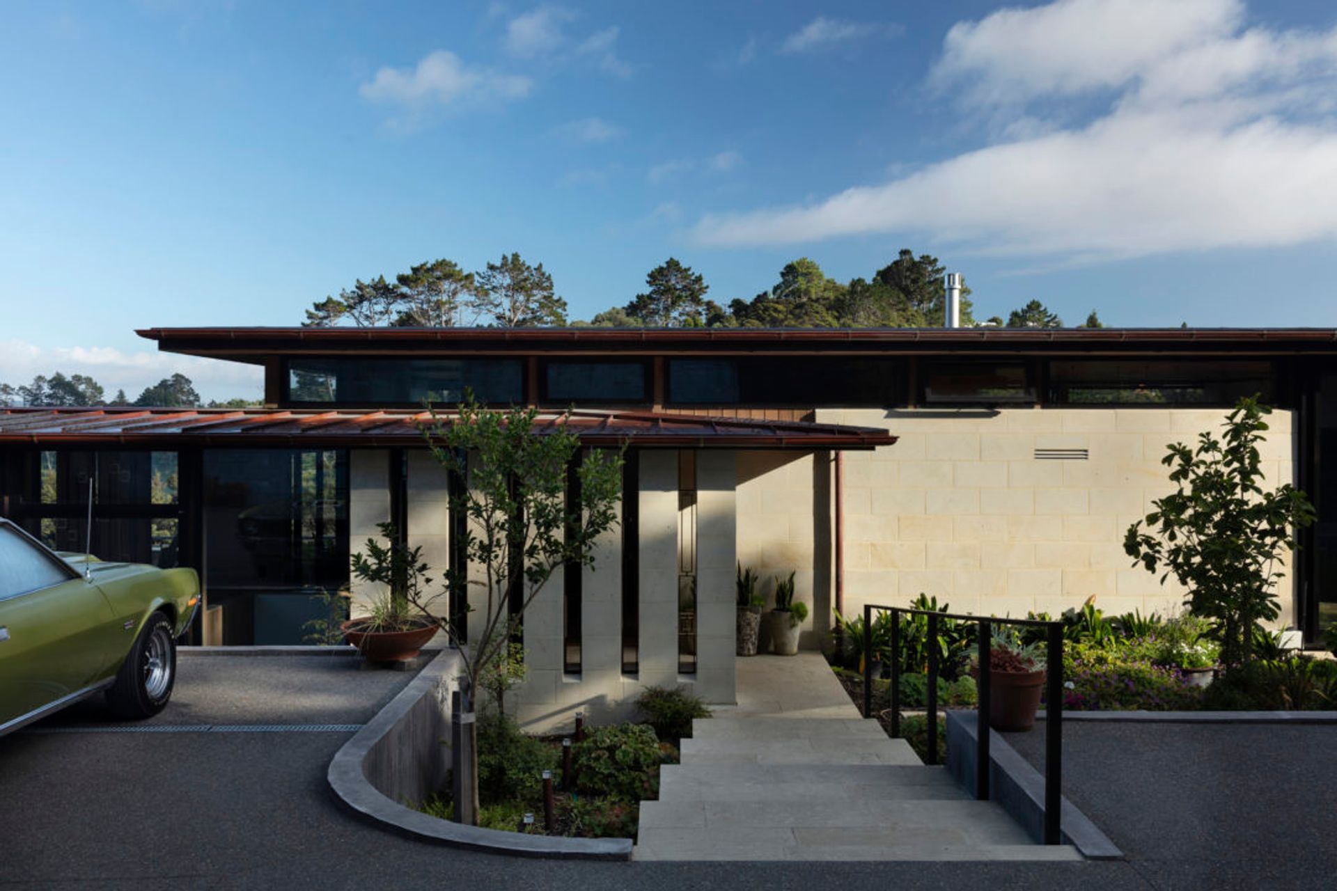 Hinuera stone on the base of the home helps to ground the building into the landscape, with gentle steps leading down to the main entrance.