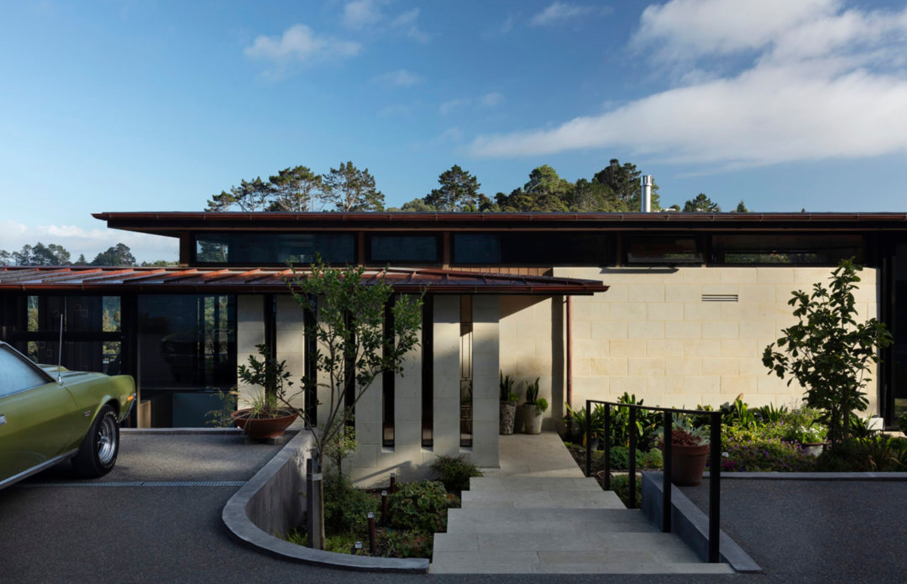 Hinuera stone on the base of the home helps to ground the building into the landscape, with gentle steps leading down to the main entrance.