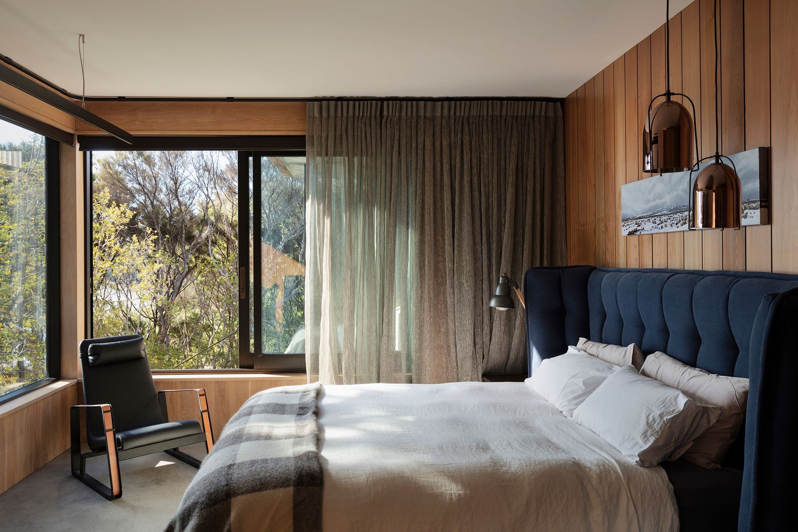 The bedroom is lined with timber panelling and enjoys views over the bush through large windows.