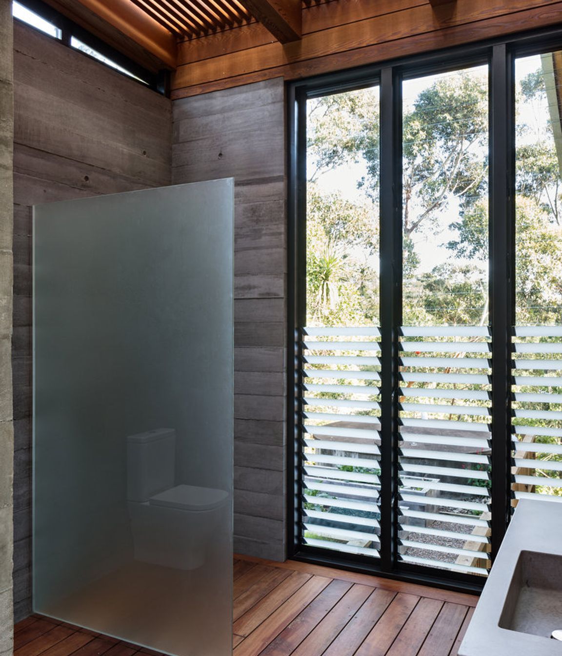 A robust bathroom features decked flooring and slatted timber ceiling.