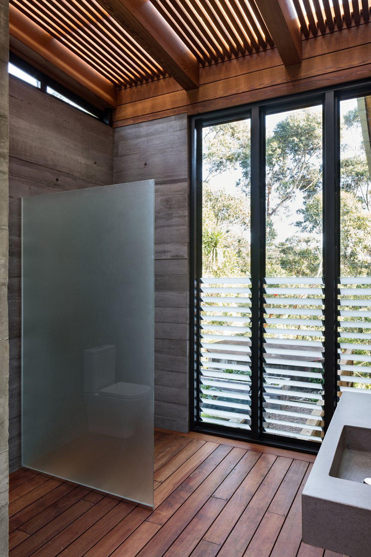 A robust bathroom features decked flooring and slatted timber ceiling.