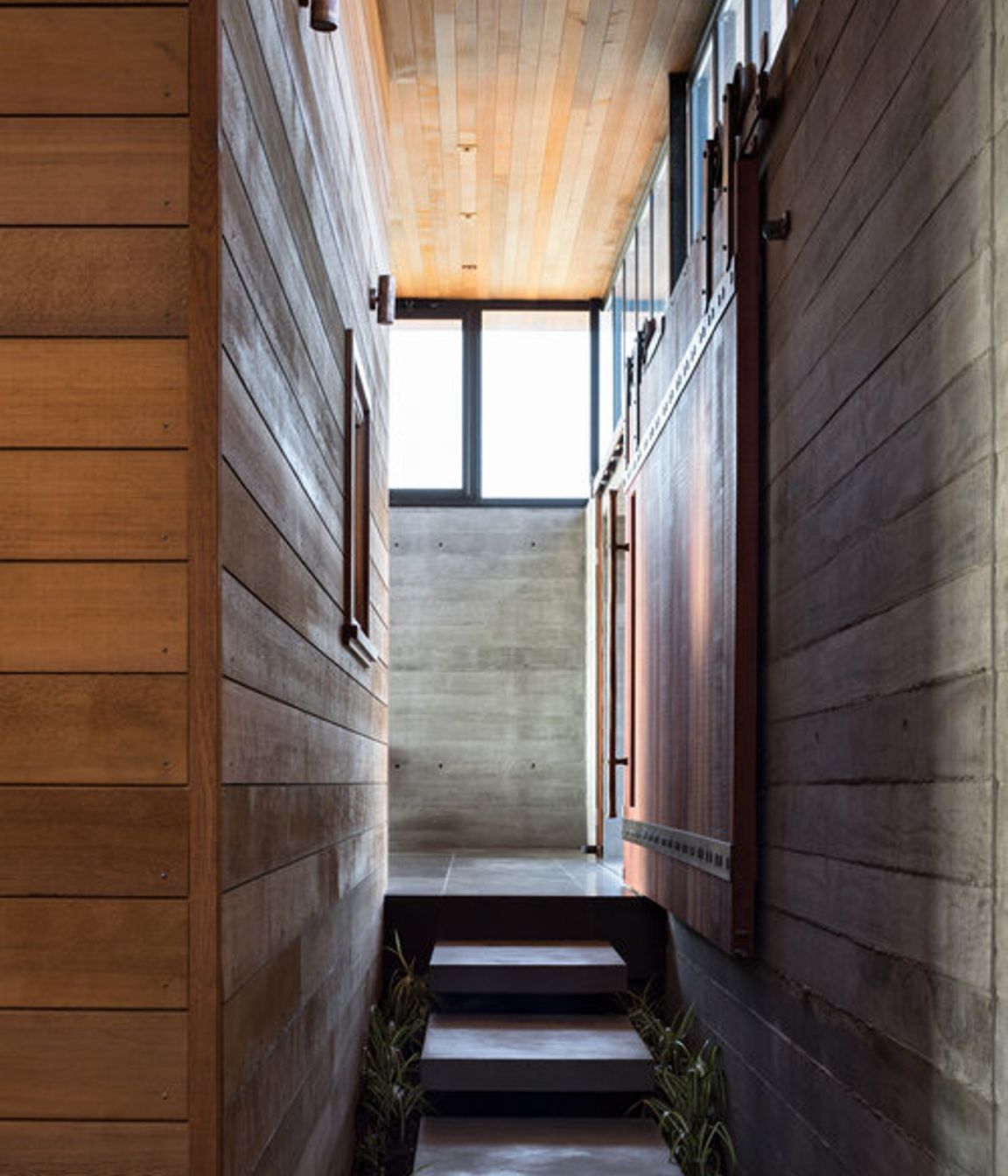 Cedar weatherboards and shuttered concrete lines the walkway to/from the courtyard.