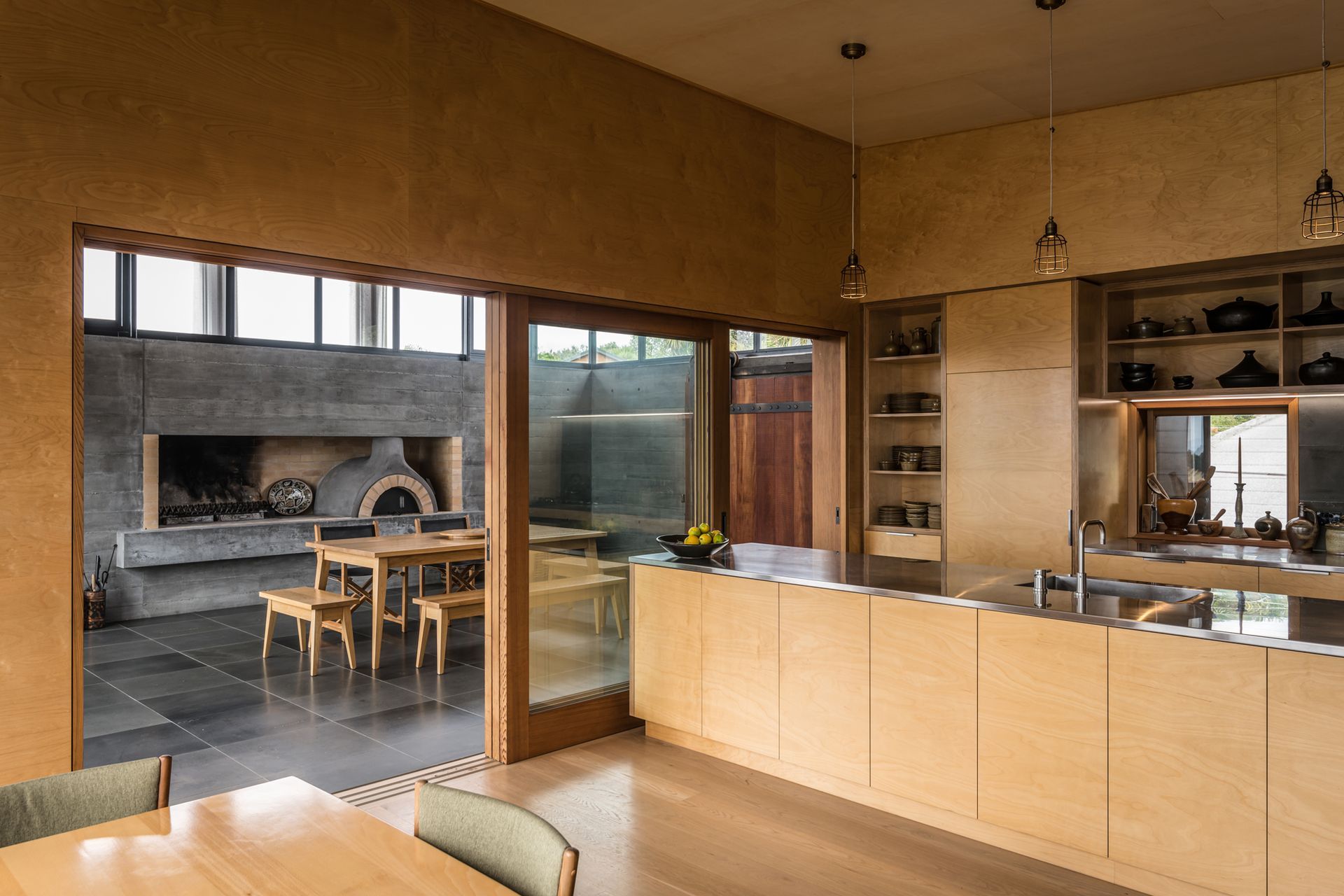 The bespoke plywood kitchen is a smooth and elegant contrast to the textured concrete and tiled floor seen in the entertainment room. Photograph by ArchiPro.