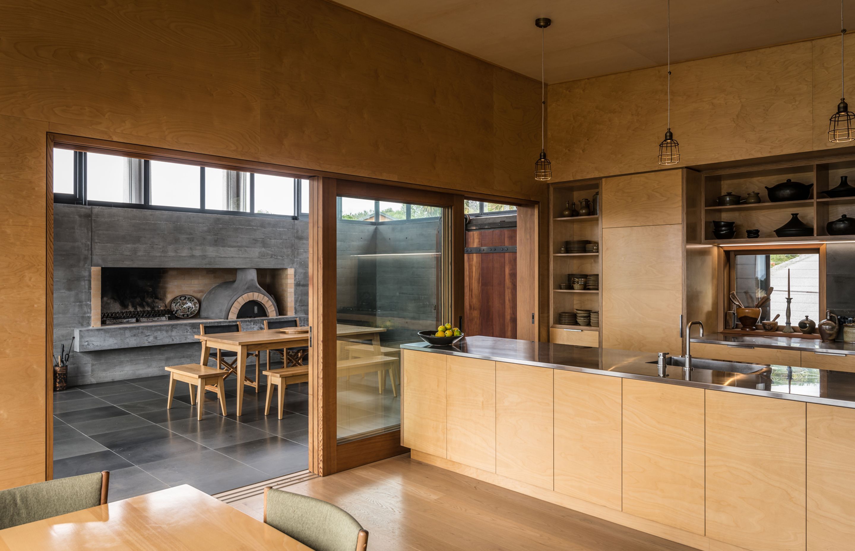 The bespoke plywood kitchen is a smooth and elegant contrast to the textured concrete and tiled floor seen in the entertainment room. Photograph by ArchiPro.