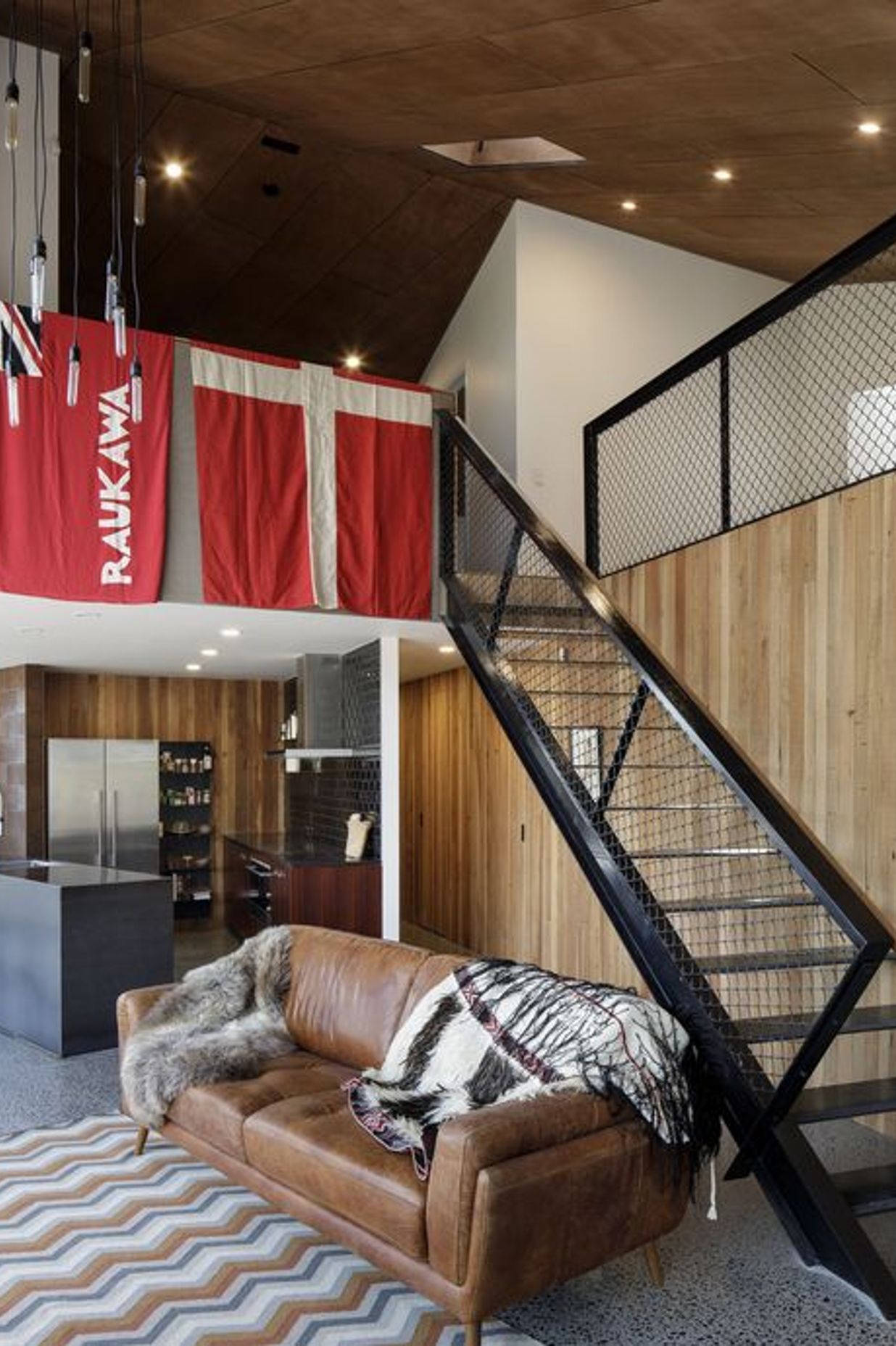 In the kitchen, stained oak-veneer cabinetry is contrasted by black gloss wall tiles, stainless steel appliances and exposed concrete flooring. 