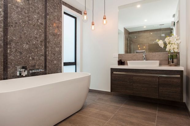 Contemporary bathroom featuring a freestanding white bathtub, wall-mounted dark wood vanity with a vessel sink, large mirror, warm pendant lights, and dark stone-look wall and floor finishes.