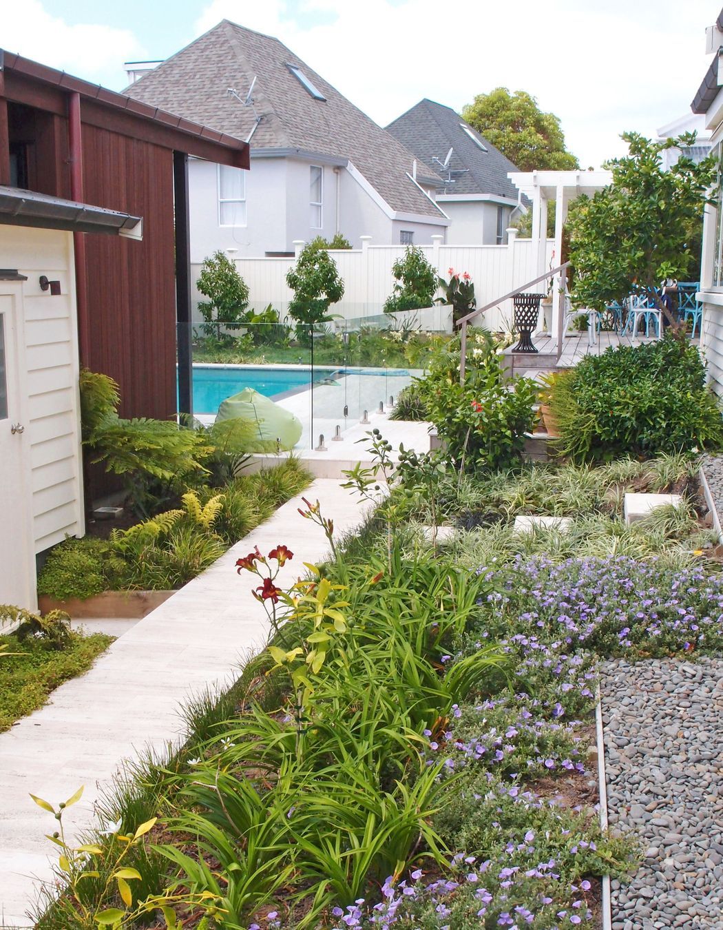 A stone tiled path leads through richly planted flowering borders to the rear garden pool courtyard