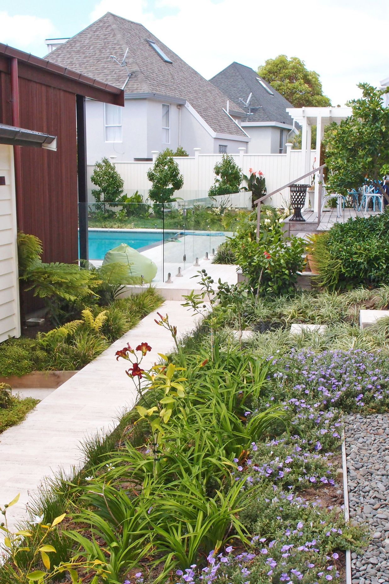 A stone tiled path leads through richly planted flowering borders to the rear garden pool courtyard