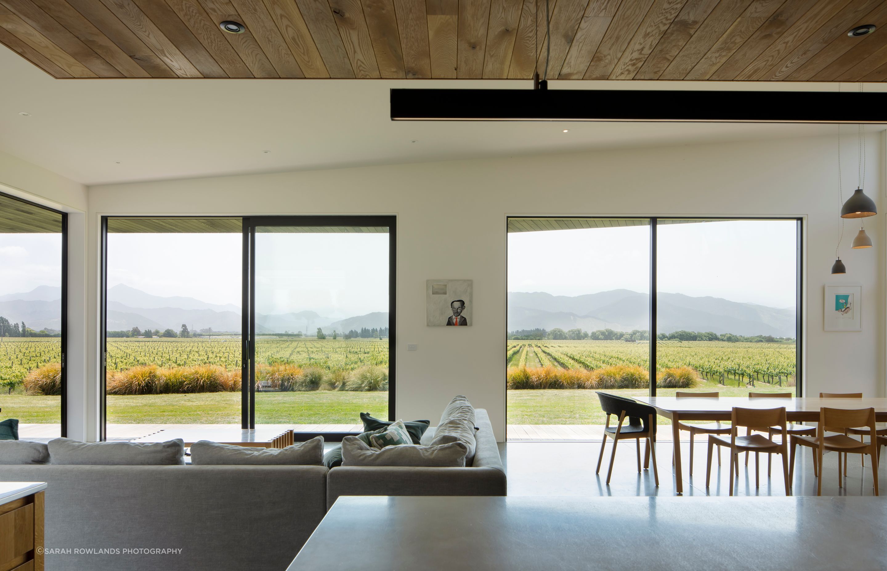 Multiple wide apertures connect the open-plan living area with the view across the valley towards the hills in the distance.
