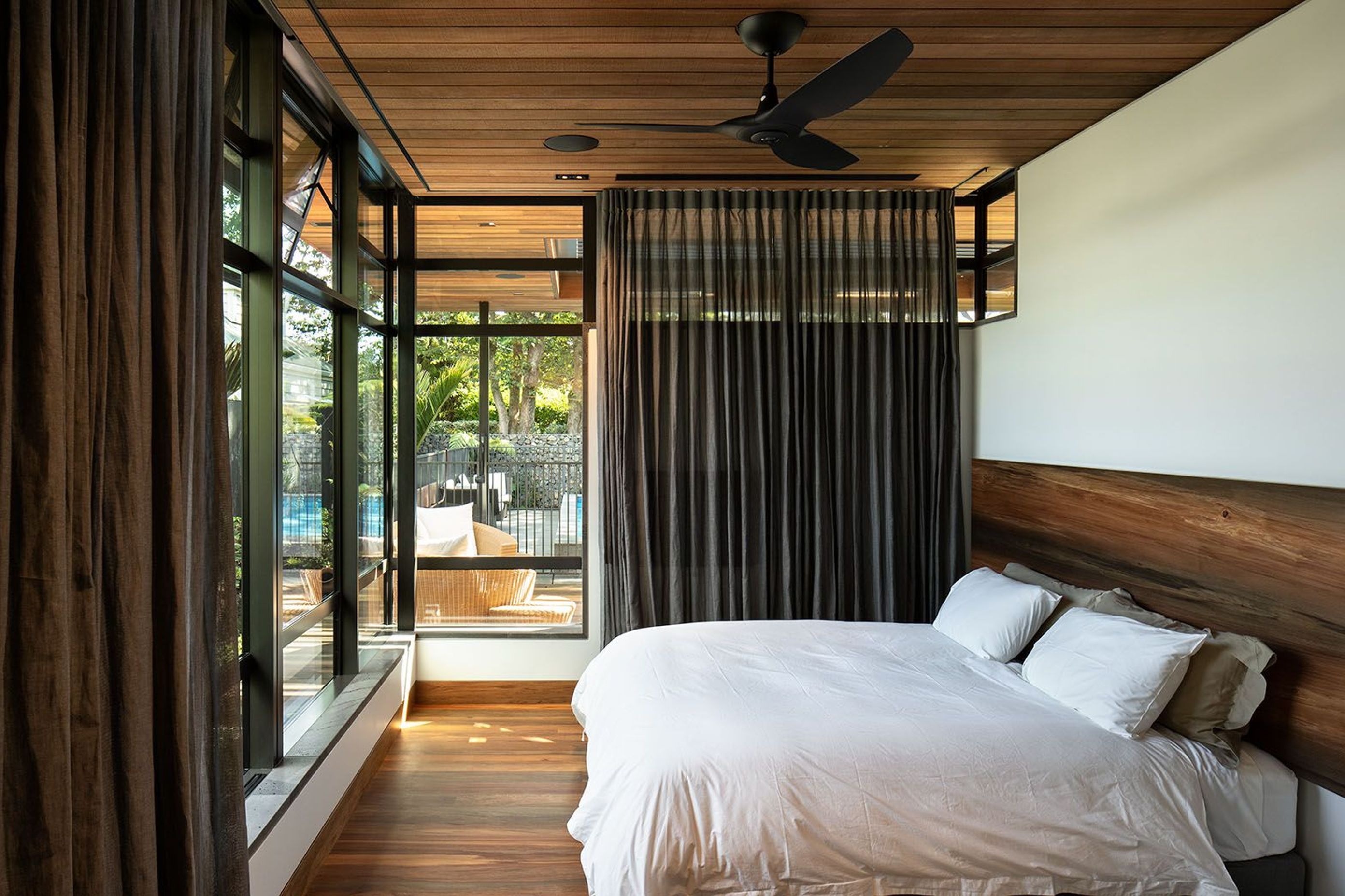 The bedroom looks out to the outdoor pool and a BBQ and seating area. The totara timber ceiling continues outside into the soffit of the exterior.