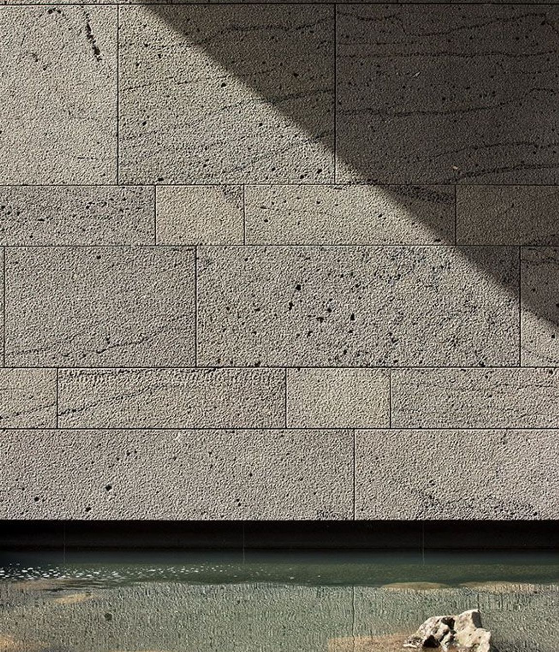 A 'bird-pecked' blue basalt stone wall is reflected in one of the reflection pools.